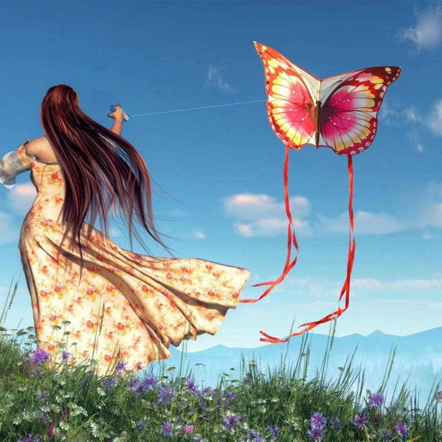 Eine Frau in einem fließenden Blumenkleid lässt einen schmetterlingsförmigen Drachen über einem grasbewachsenen Feld fliegen, mit Bergen und blauem Himmel im Hintergrund.