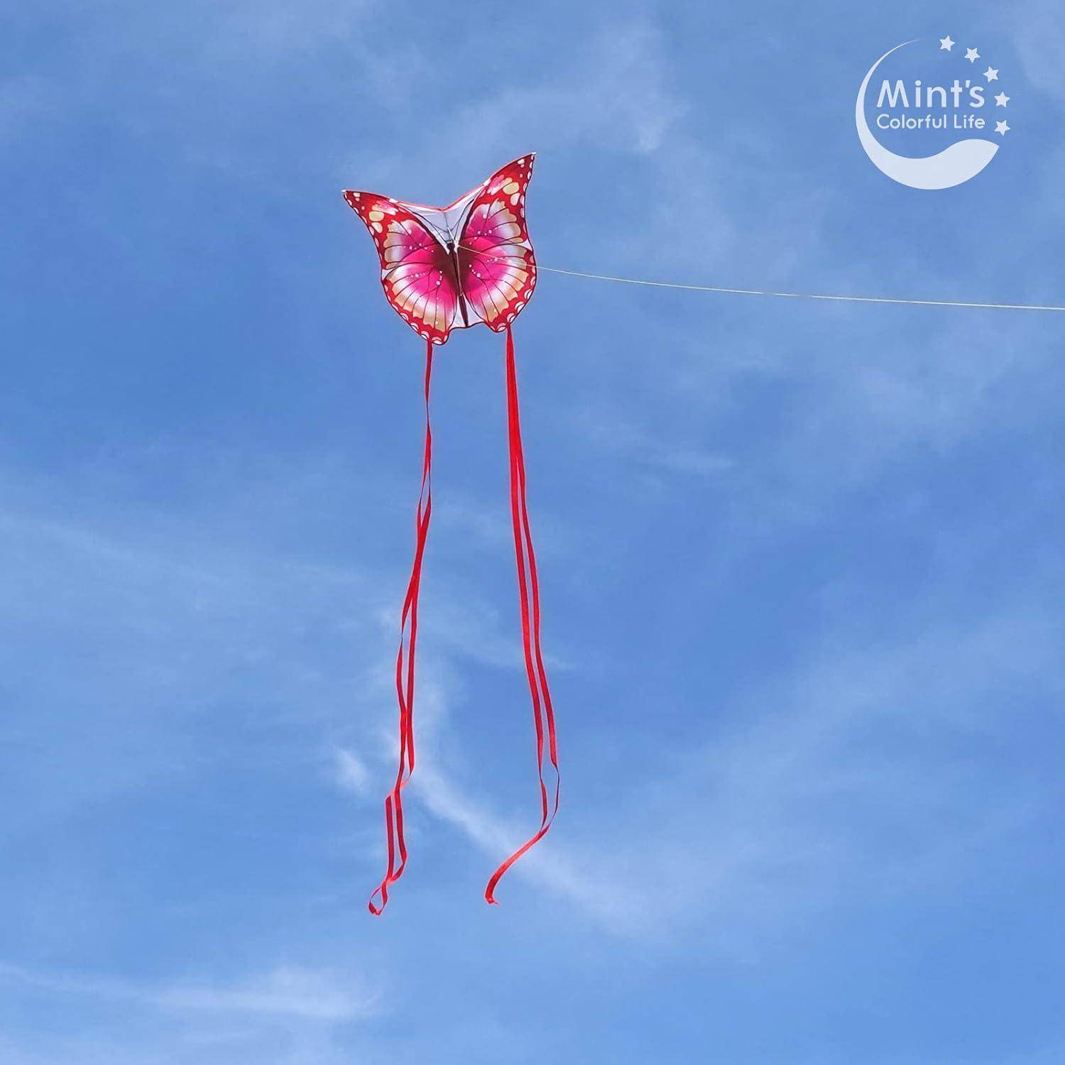 Ein rosa schmetterlingsförmiger Drachen mit langen roten Bändern fliegt gegen einen blauen Himmel.