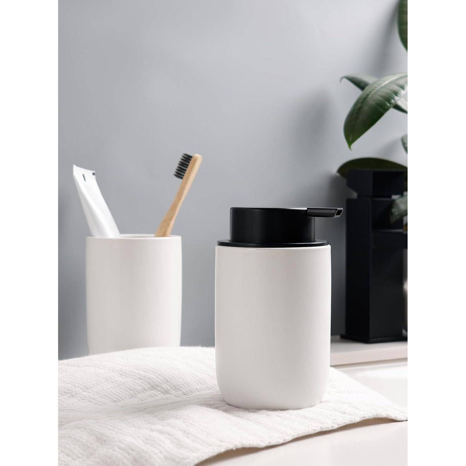 Minimalistischer Badezimmertisch mit zwei weißen Behältern mit Zahnbürsten, neben einem Behälter mit schwarzem Deckel und einer kleinen Pflanze.