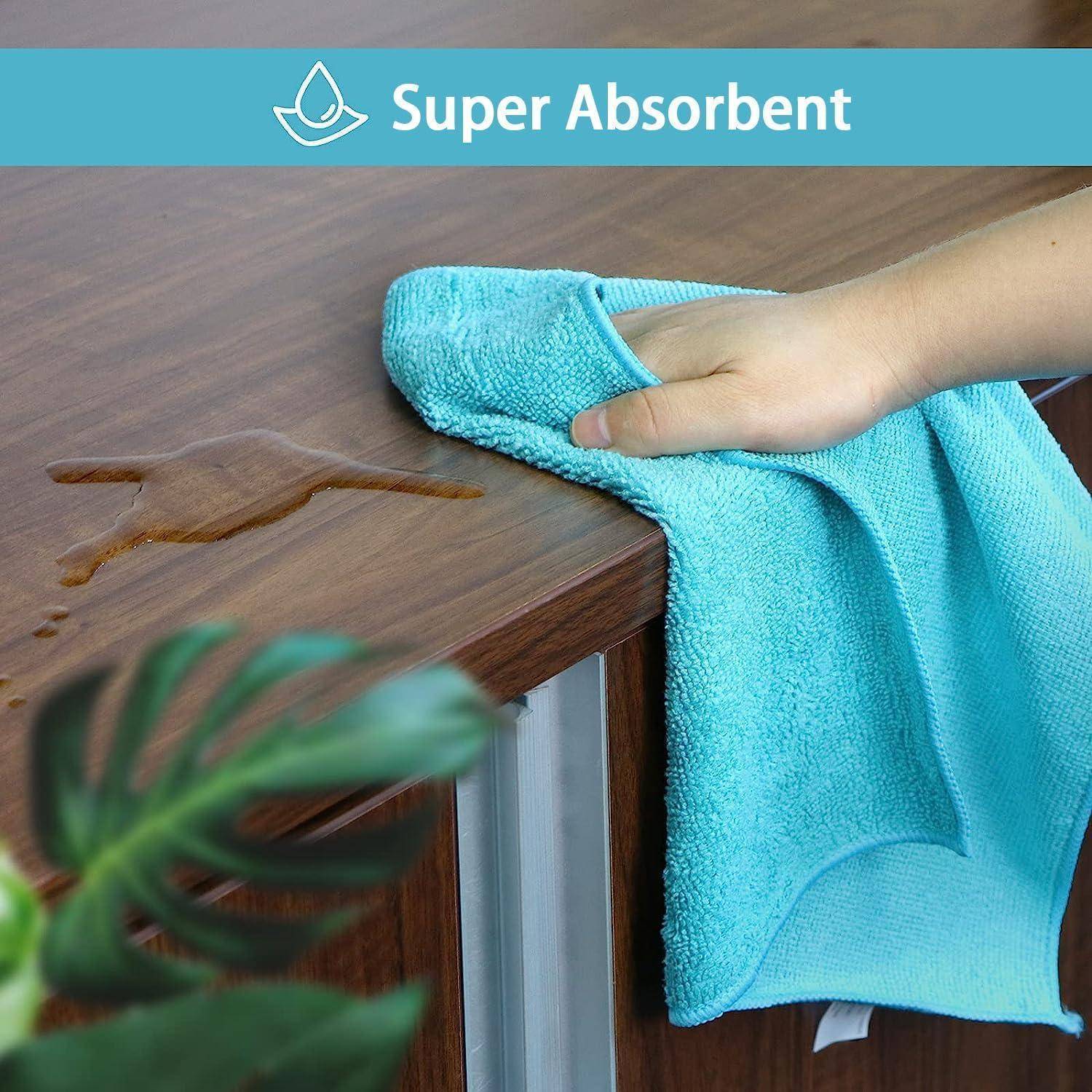 Hand wischt verschüttete Flüssigkeit von einem Holztisch mit einem blauen Mikrofasertuch ab; Text liest „Super Absorbent
