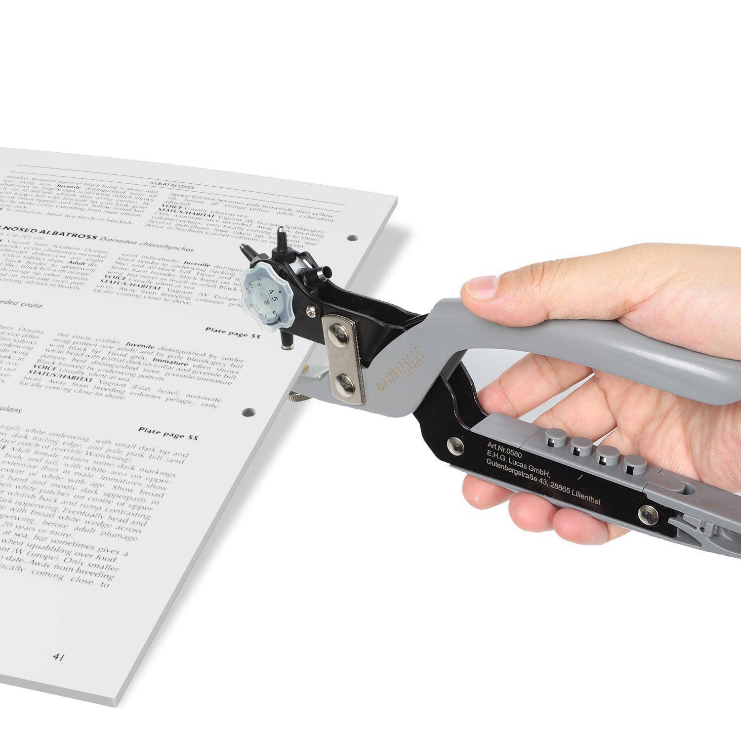 Eine Hand benutzt ein metallisches Buchlochwerkzeug, um Löcher in einen Stapel gedruckter Seiten auf weißem Hintergrund zu stanzen.