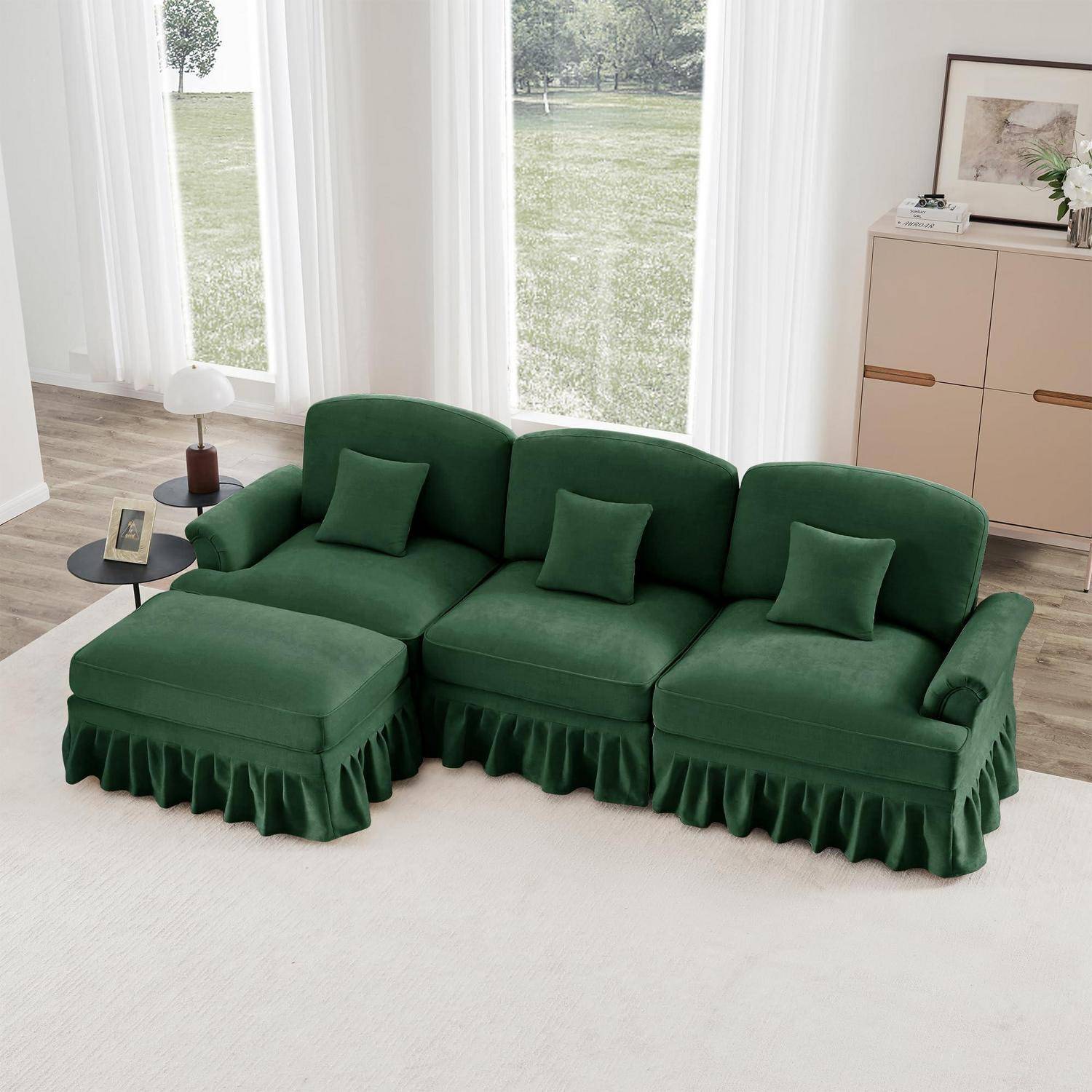 Grünes modulares Sofa mit Rüschensaum und passendem Hocker in einem hellen Wohnzimmer, mit kleinen Beistelltischen und großen Fenstern.