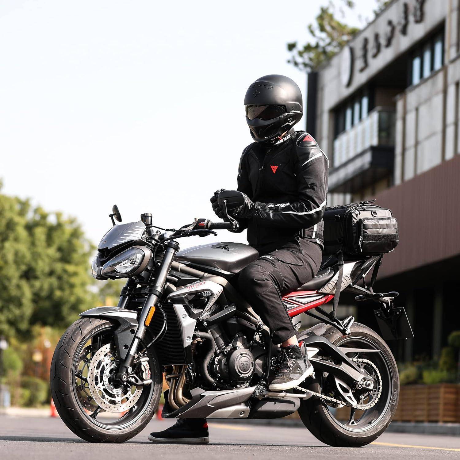 Motorradfahrer in schwarzer Ausrüstung und Helm sitzt auf einem geparkten Sportmotorrad auf einer Straße neben einem Gebäude.