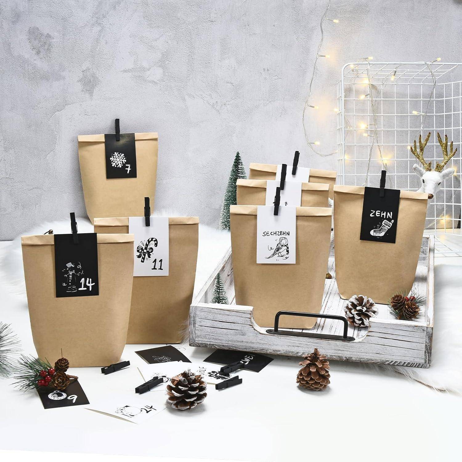 Adventskalender-Geschenktüten mit den Nummern 7, 9, 11, 14 und 24, angeordnet auf einem weißen Holztablett mit Tannenzapfen und Winterdekoration.