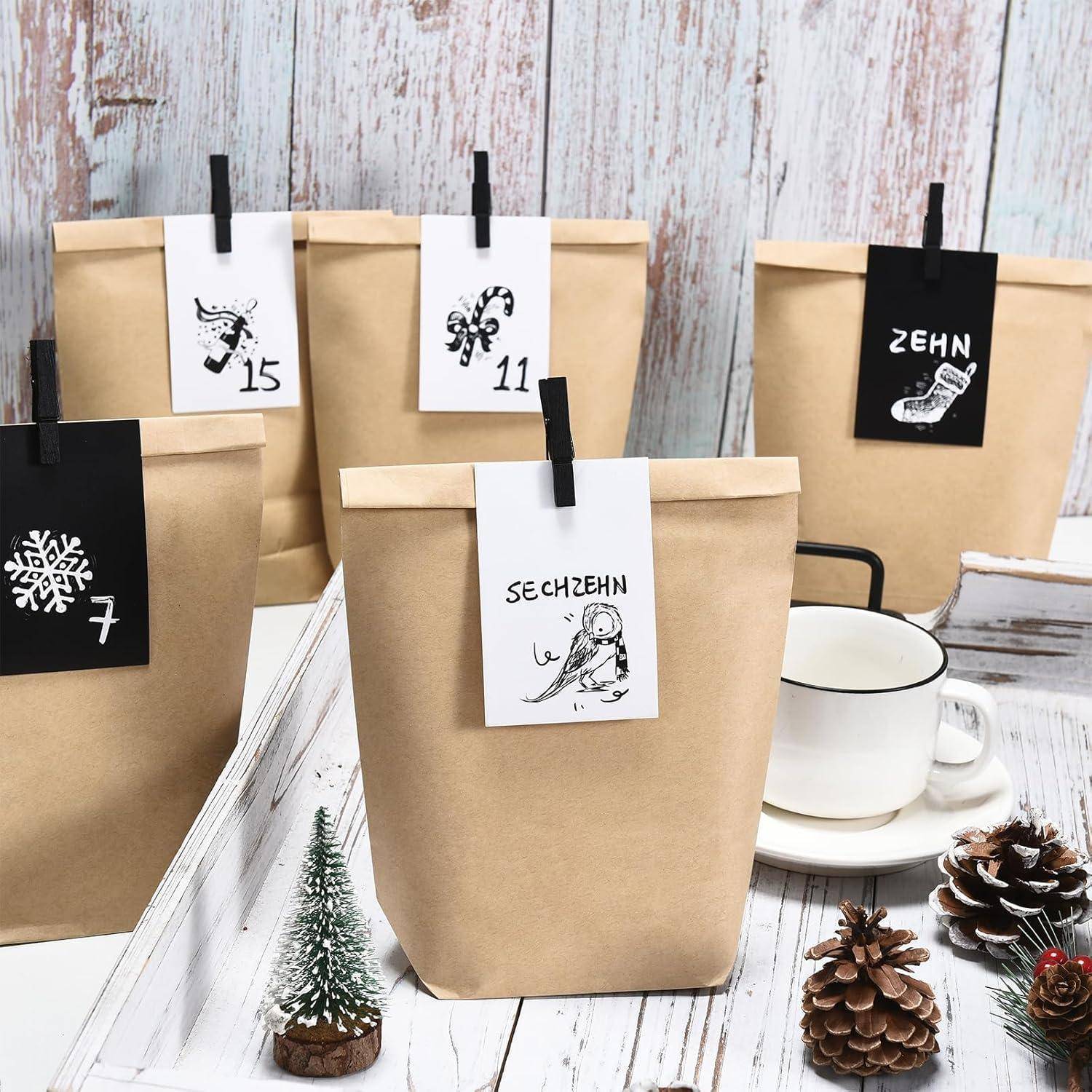 Fünf Kraftpapiertüten mit hängenden nummerierten Schildern, angeordnet wie ein Adventskalender; eine weiße Tasse, Tannenzapfen und ein kleiner Baum schmücken die Szene.