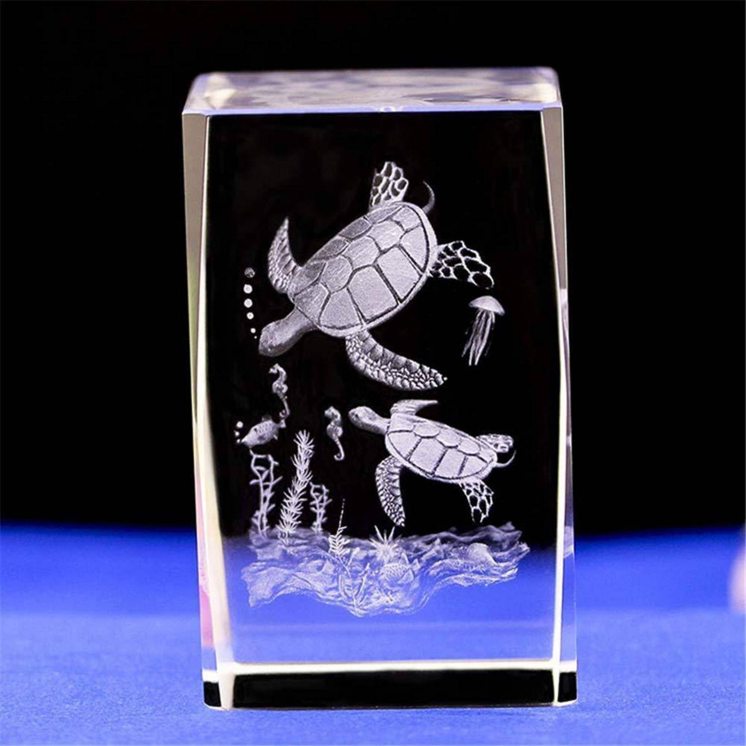 3D-Glasblock mit gravierten Meeresschildkröten und Unterwasserpflanzen auf schwarzem Hintergrund.