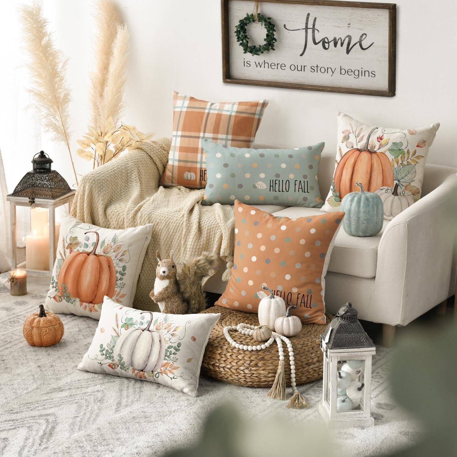 Herbstlich dekoriertes Wohnzimmer mit Kissen, Laternen, Kürbissen und einem Wandschild mit der Aufschrift „Zuhause ist, wo unsere Geschichte beginnt