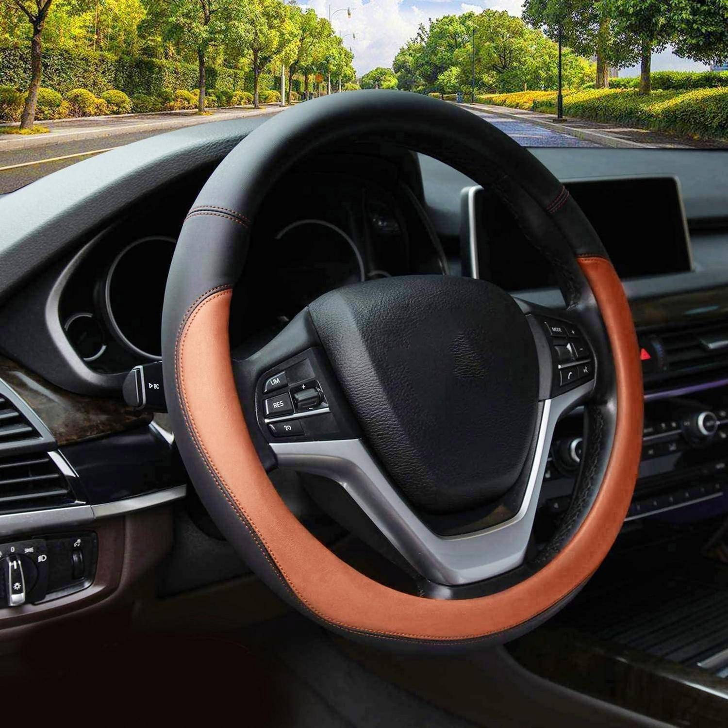 Autoinnenraum mit einer Nahaufnahme eines Lenkrads, das in braun und schwarzem Leder umwickelt ist, Armaturenbrett und Touchscreen sind sichtbar, geparkt auf einer baumbestandenen Straße.