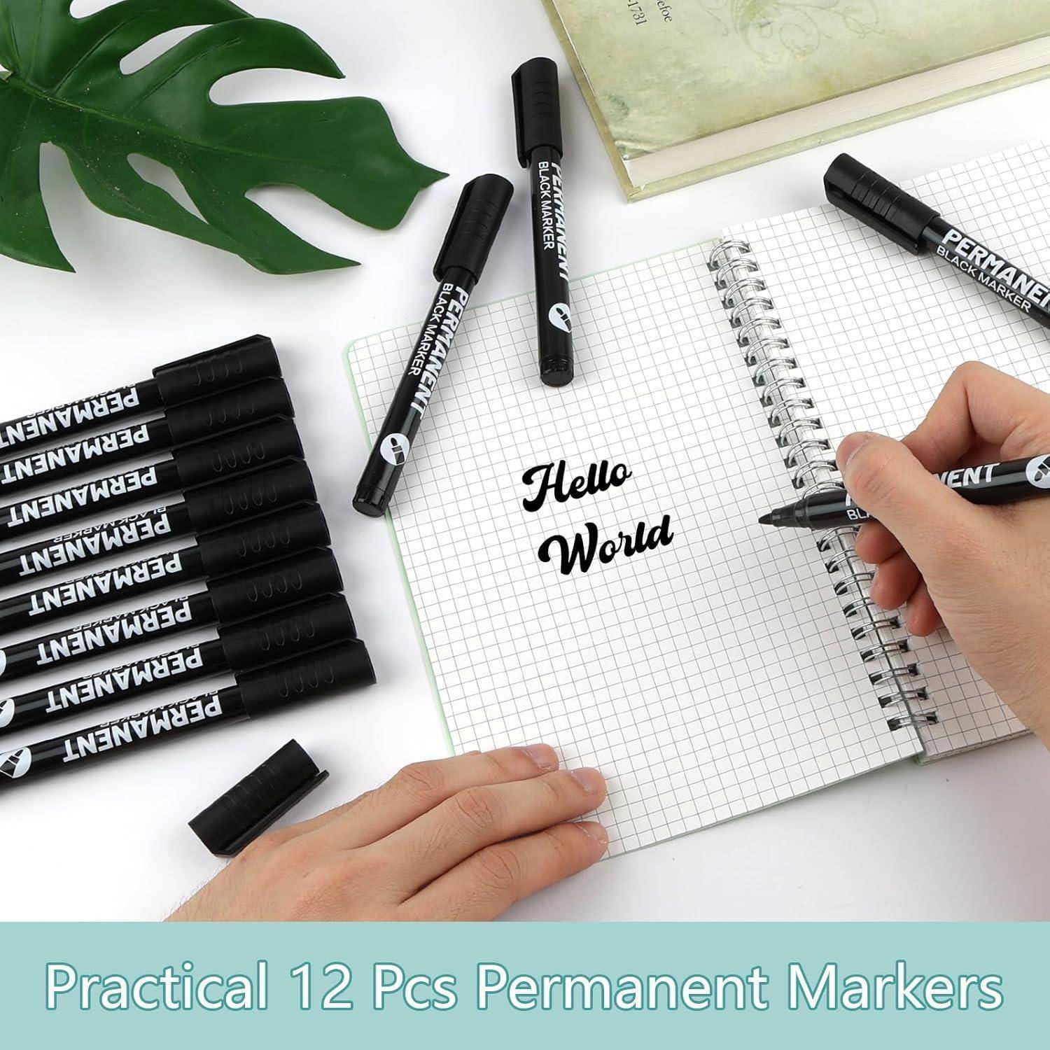 Handschrift 'Hallo Welt' in einem Spiralblock mit einem Permanentmarker geschrieben, umgeben von schwarzen Markern und einem grünen Blatt auf einem weißen Schreibtisch.