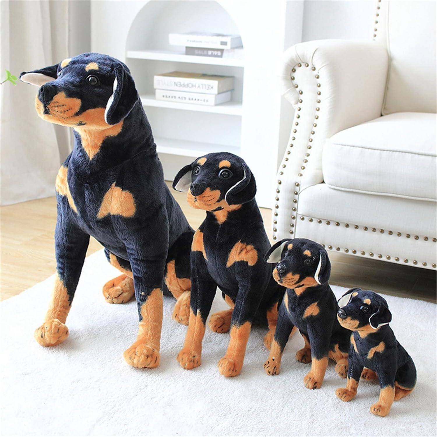 Vier kuschelweiche schwarz-lohfarbene Hundespielzeuge der Größe nach von größt zu kleinst auf einem weißen Teppich in einem hellen Wohnzimmer arrangiert.