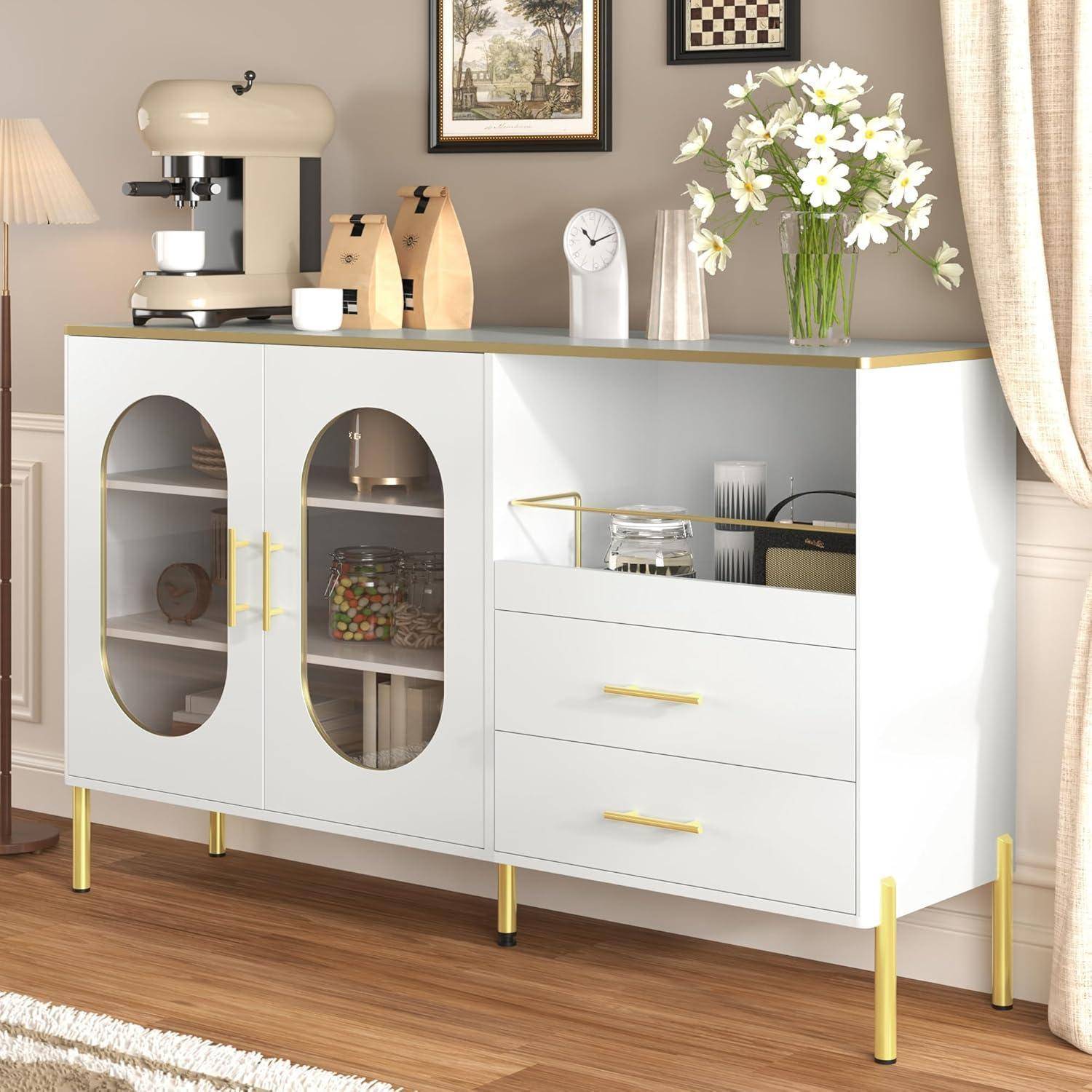 Modernes weißes Sideboard mit goldfarbenen Beinen und Griffen, auf dem eine Kaffeemaschine, Dekorationsgegenstände, eine Uhr, Blumen und Küchenutensilien in einem hellen Raum stehen.