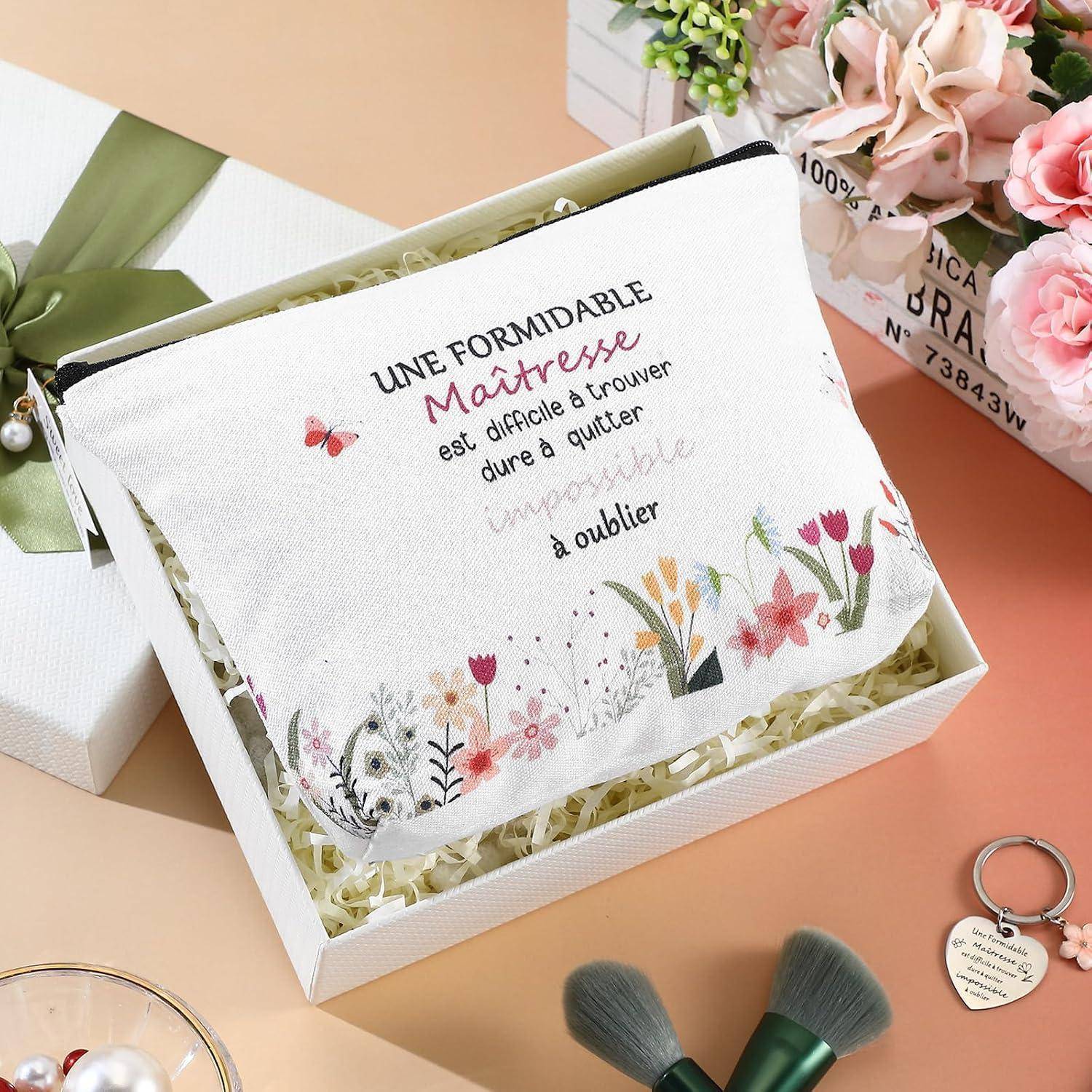 Geschenkbox mit einem dekorativen Beutel, bestickt auf Französisch: 'UNE FORMIDABLE MAÎTRESSE est difficile à trouver dure à quitter impossible à oublier', mit floralen Akzenten und einem Schmetterling.