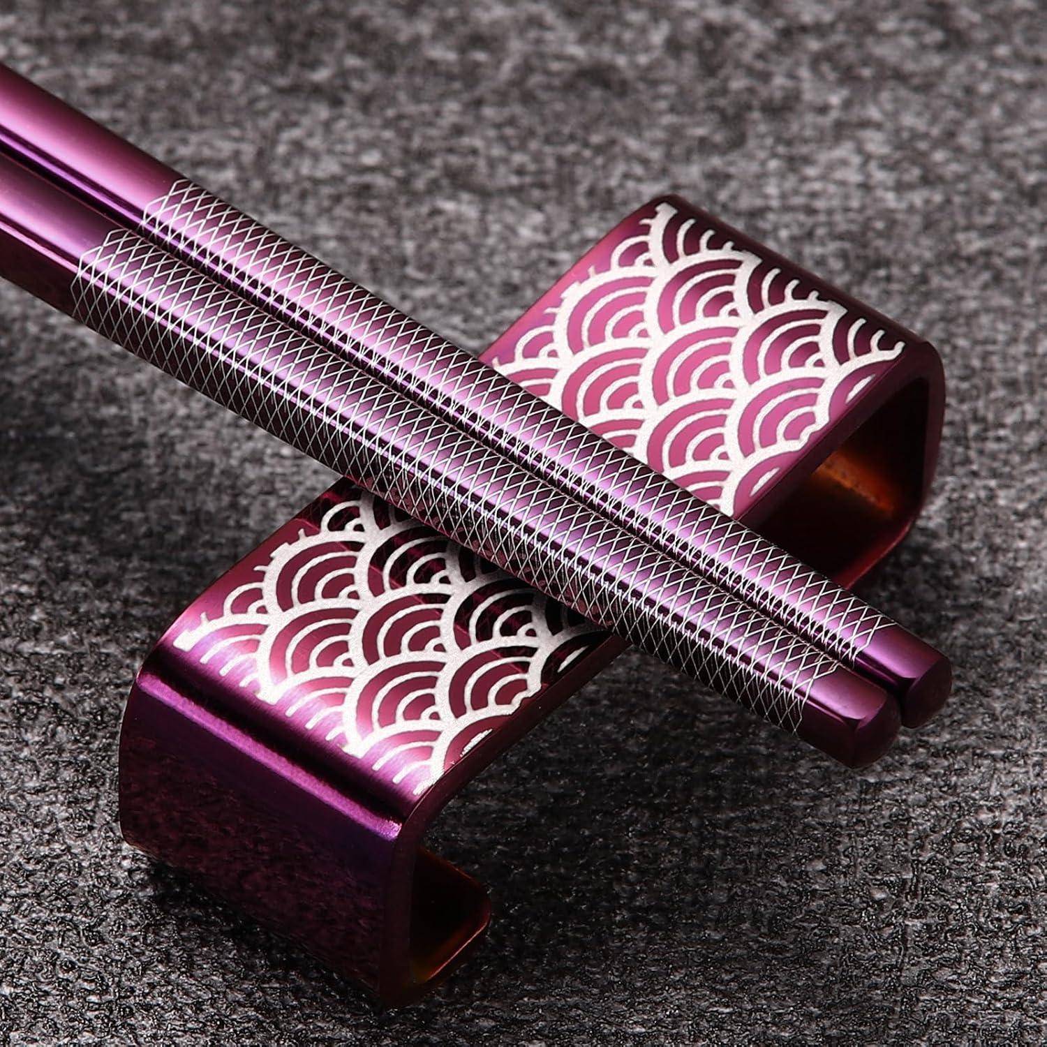 Zwei metallische lila Essstäbchen ruhen diagonal auf einem passenden dekorativen Ständer mit weißen Wellenmuster auf einer strukturierten grauen Oberfläche.