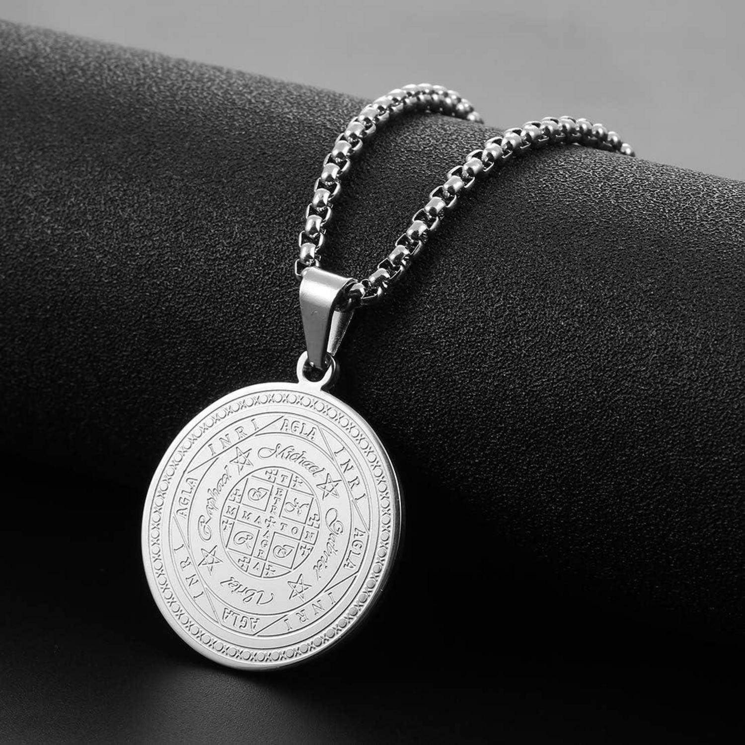 Silberner runder Anhängerschmuck mit eingravierter mystischer Symbolik und einer Kette, die über einen schwarzen Präsentationsständer drapiert ist.