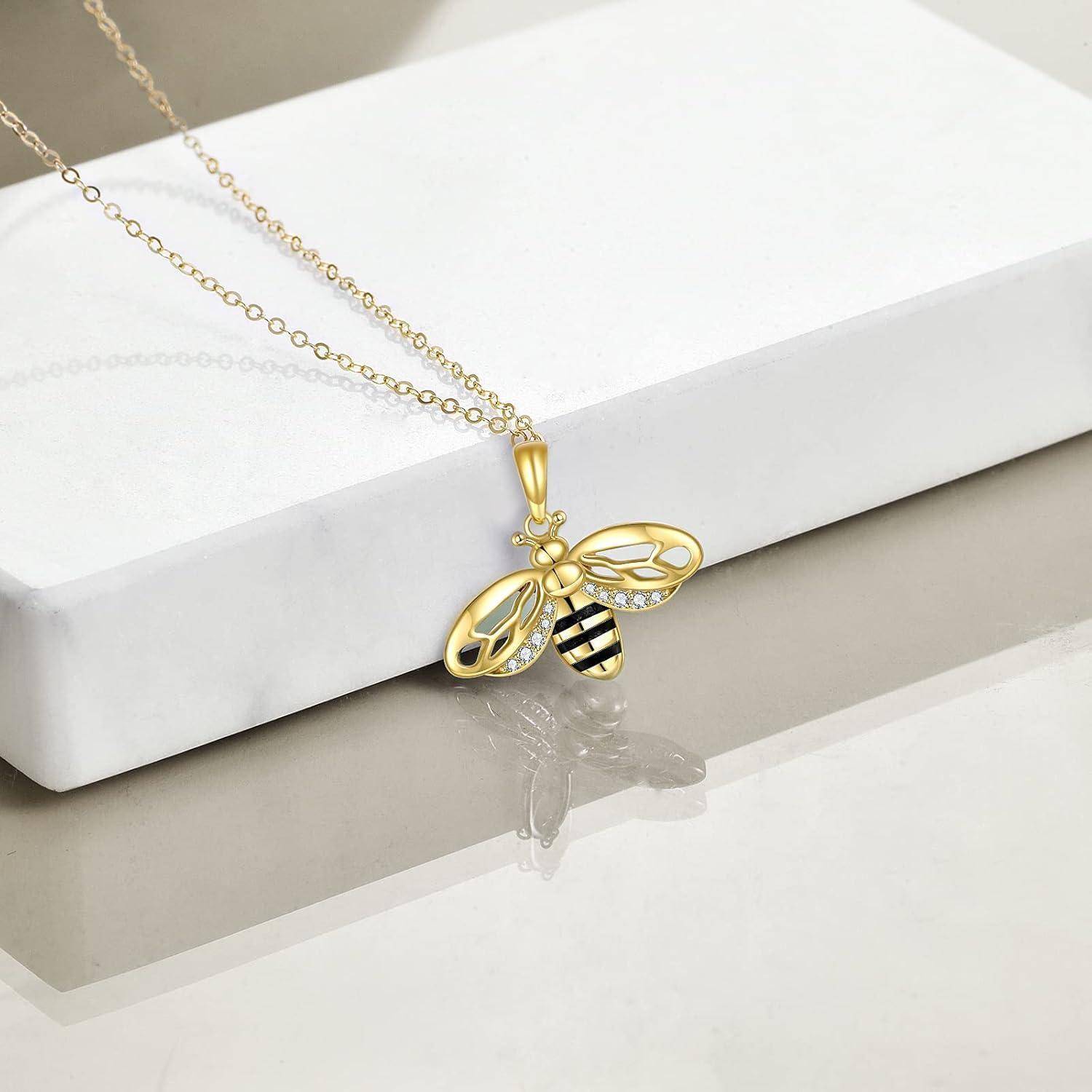 Goldene Bienen-Anhänger-Halskette mit einem gestreiften Bienen-Charm und klaren Flügeldetails an einer zierlichen Kette, ausgestellt auf einer weißen Schachtel.