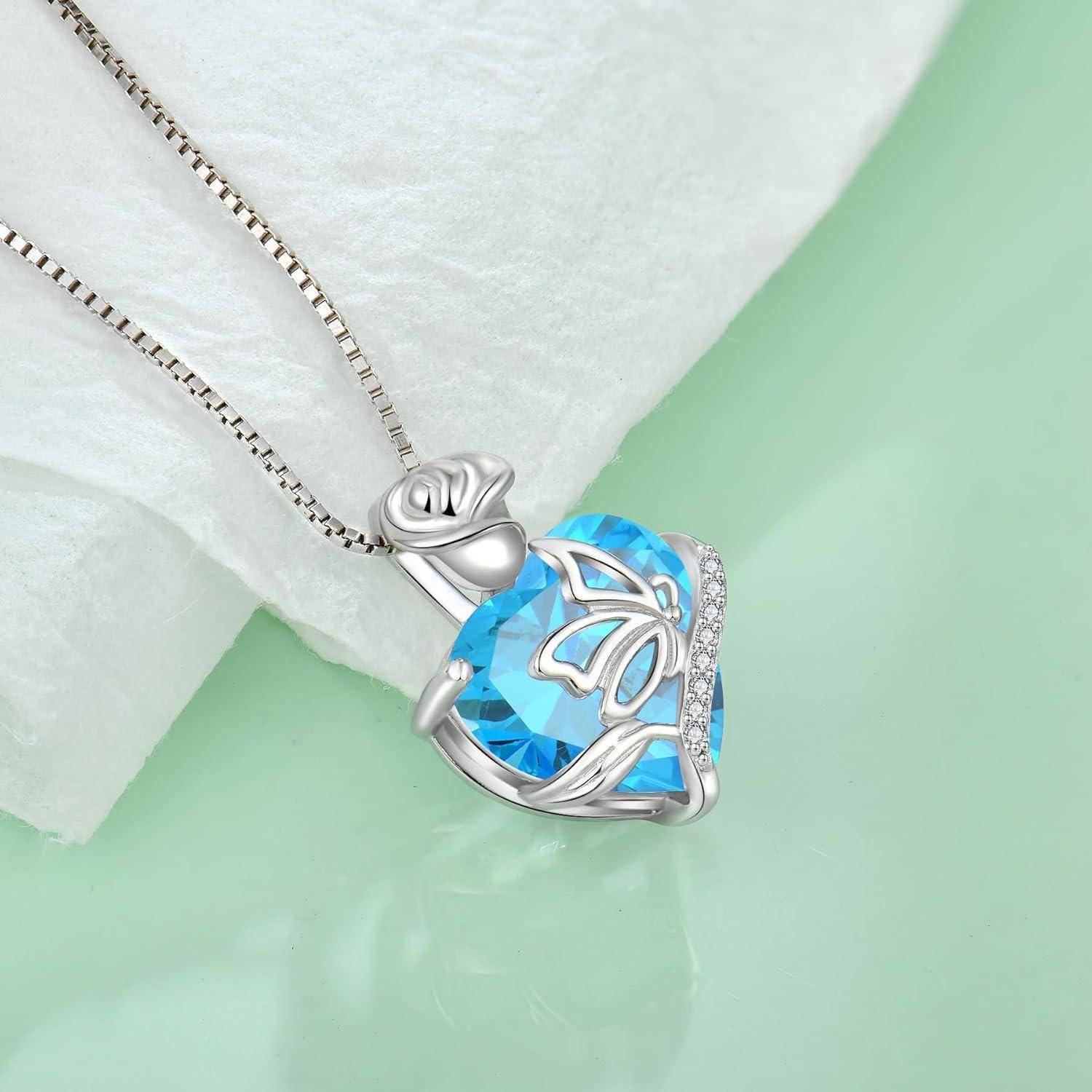 Silberner Anhängerkette mit einem blauem herzförmigen Edelstein und Schmetterlingsdesign an einer zarten Kette, präsentiert auf einem weichen weißen Kissen.