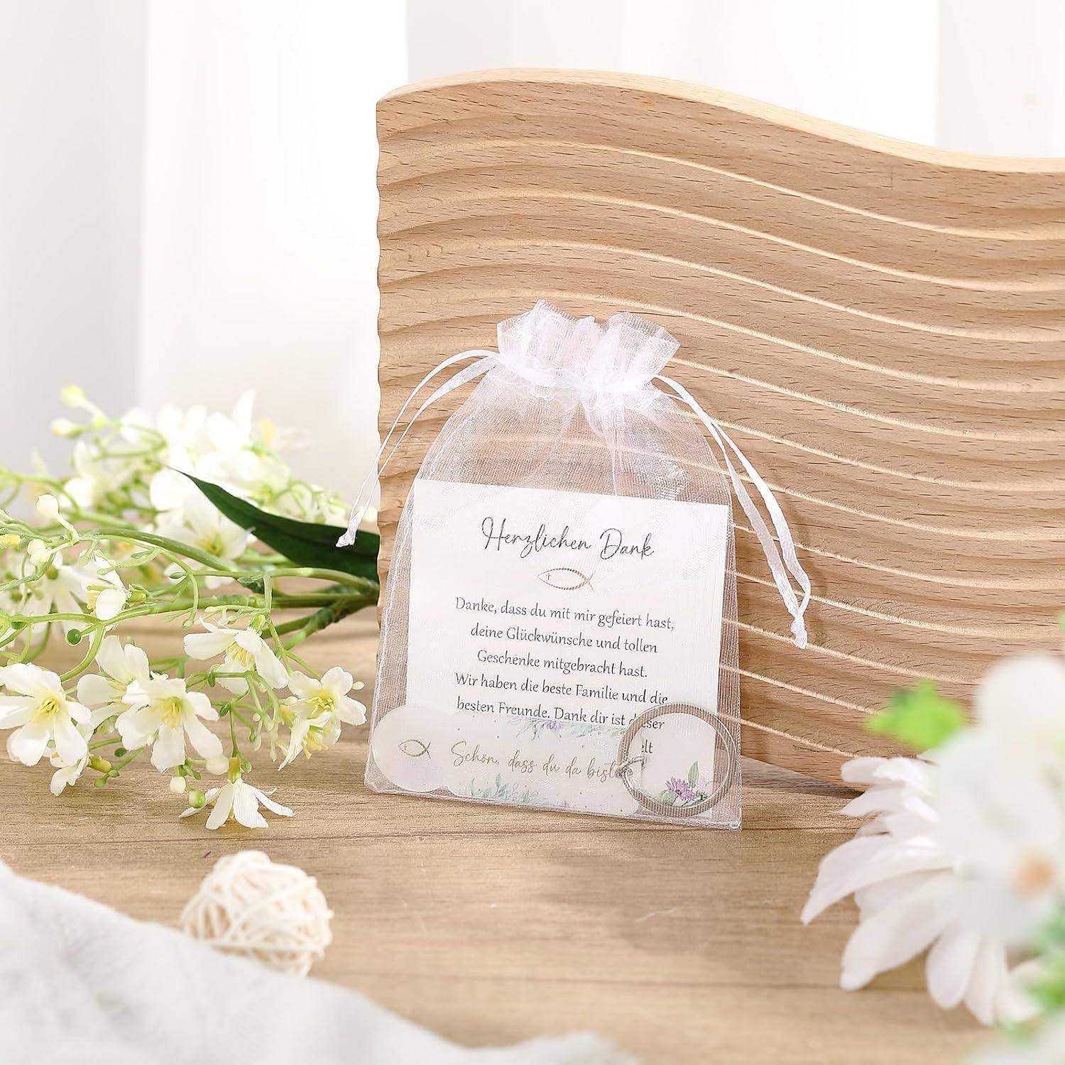 Kleine weiße Organza-Geschenktasche mit einer Dankeskarte und einem Ring, präsentiert auf einer Holzoberfläche mit weißen Blumen und einem gewellten Holzhintergrund.