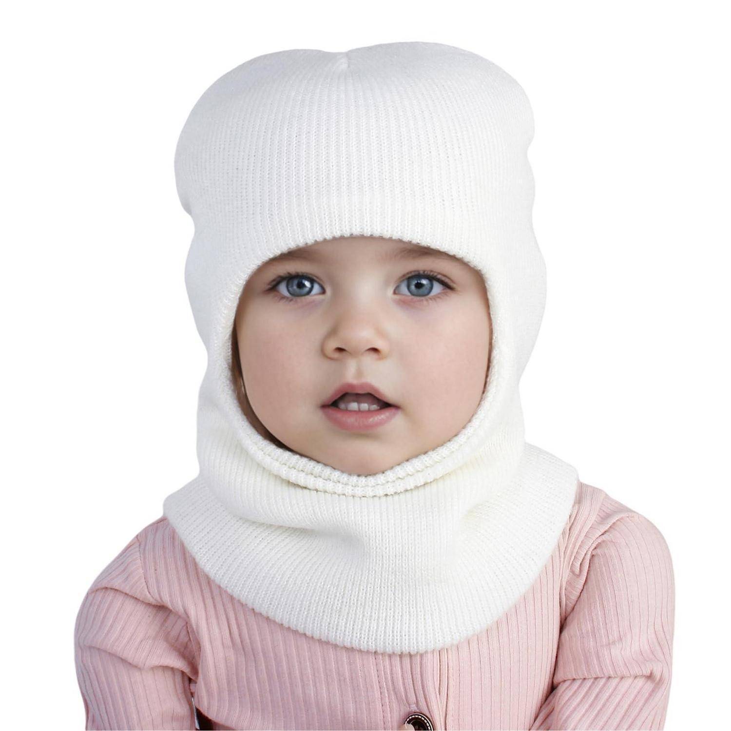 Nahaufnahme eines Babys, das eine weiße gestrickte Wintermütze und einen passenden Halswärmer über einem rosa Oberteil vor weißem Hintergrund trägt.