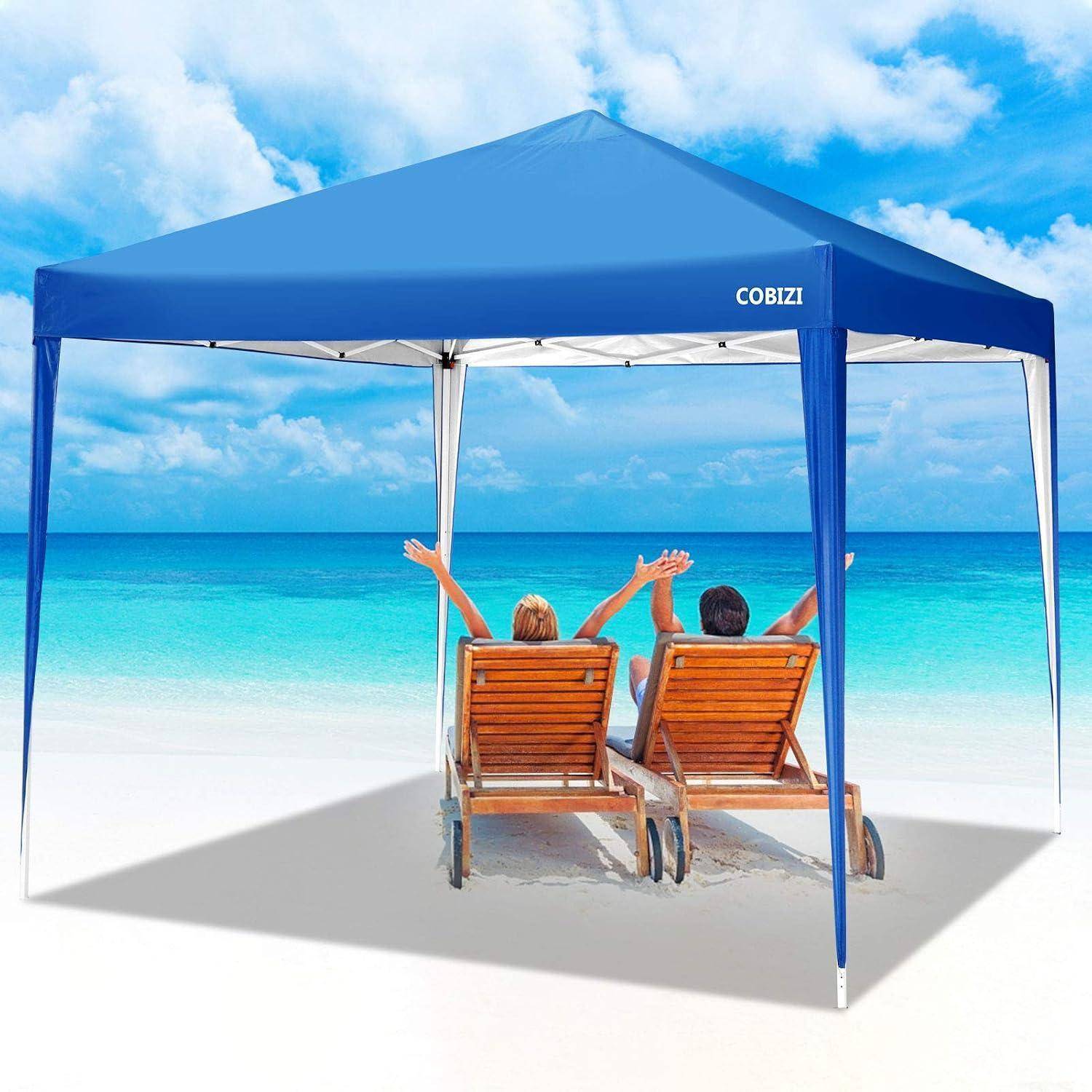 Zwei Personen entspannen sich in hölzernen Strandliegen unter einem blauen Sonnenschirm-Zelt der Marke "COBIZI"" an einem sonnigen weißen Sandstrand neben türkisblauem Wasser.