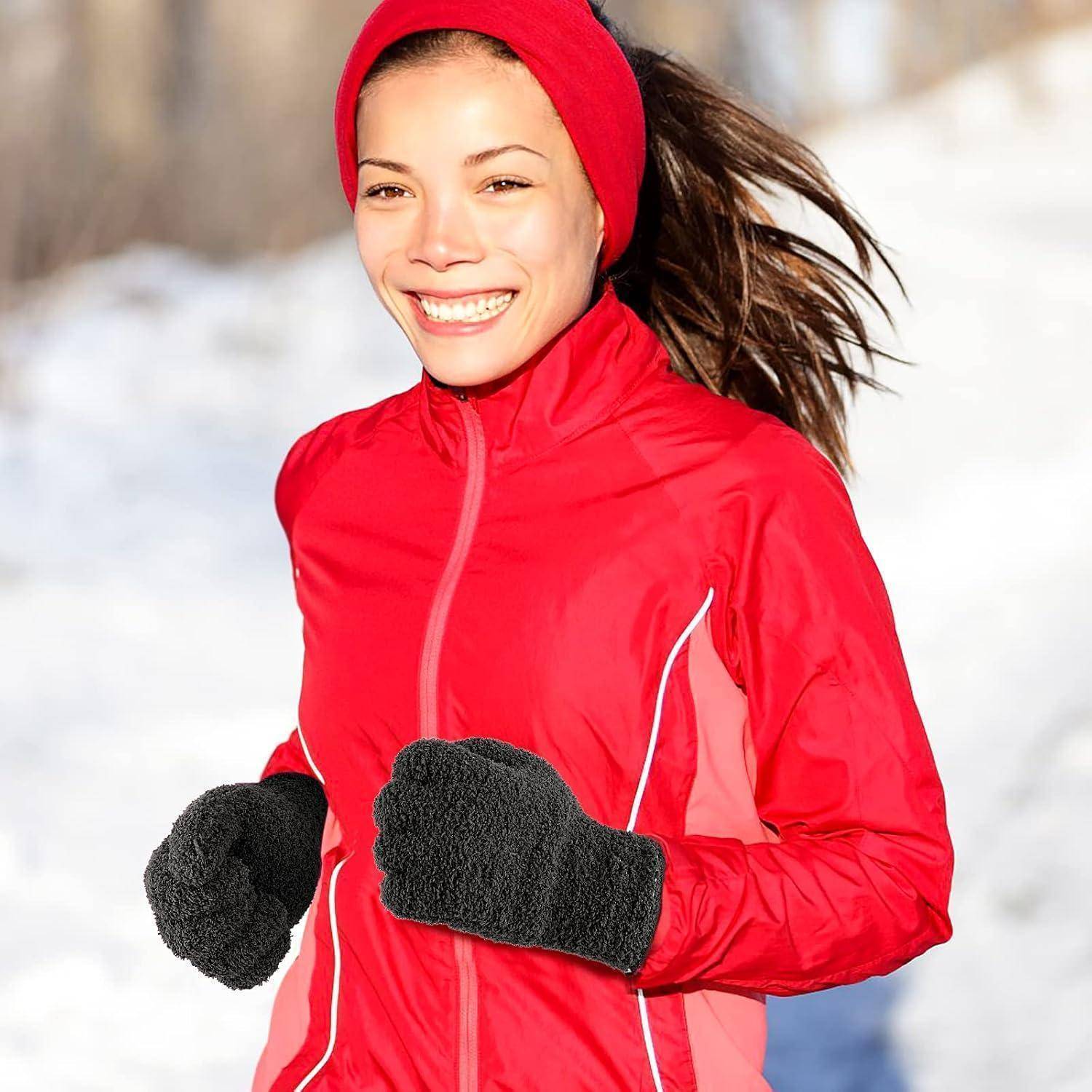 Lachende Frau in einer roten Winterjacke, Mütze und Handschuhen, die im Schnee draußen joggt.