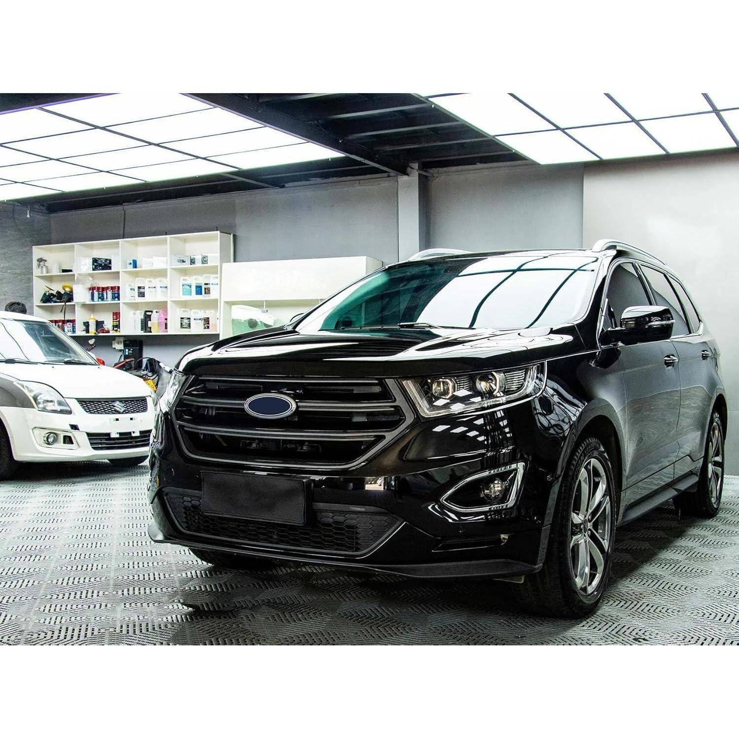 Schwarzes SUV-Fahrzeug in einer Ausstellungshalle geparkt, mit einem weißen Auto daneben und Regalen mit Produkten im Hintergrund.
