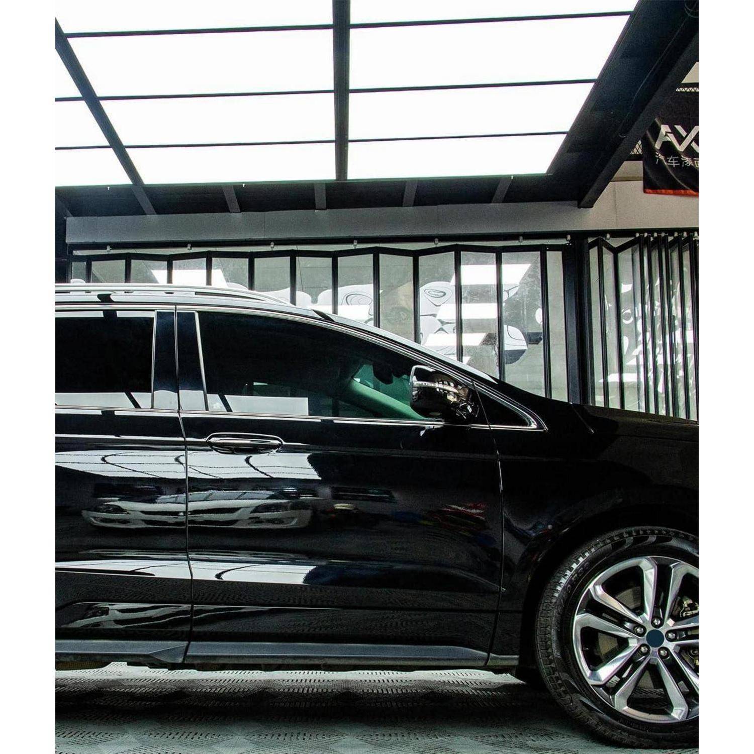 Seitenansicht eines schwarzen SUV, der in einem Innenbereich unter einem Glasdach geparkt ist und getönte Fenster sowie ein großes Leichtmetallrad zeigt.