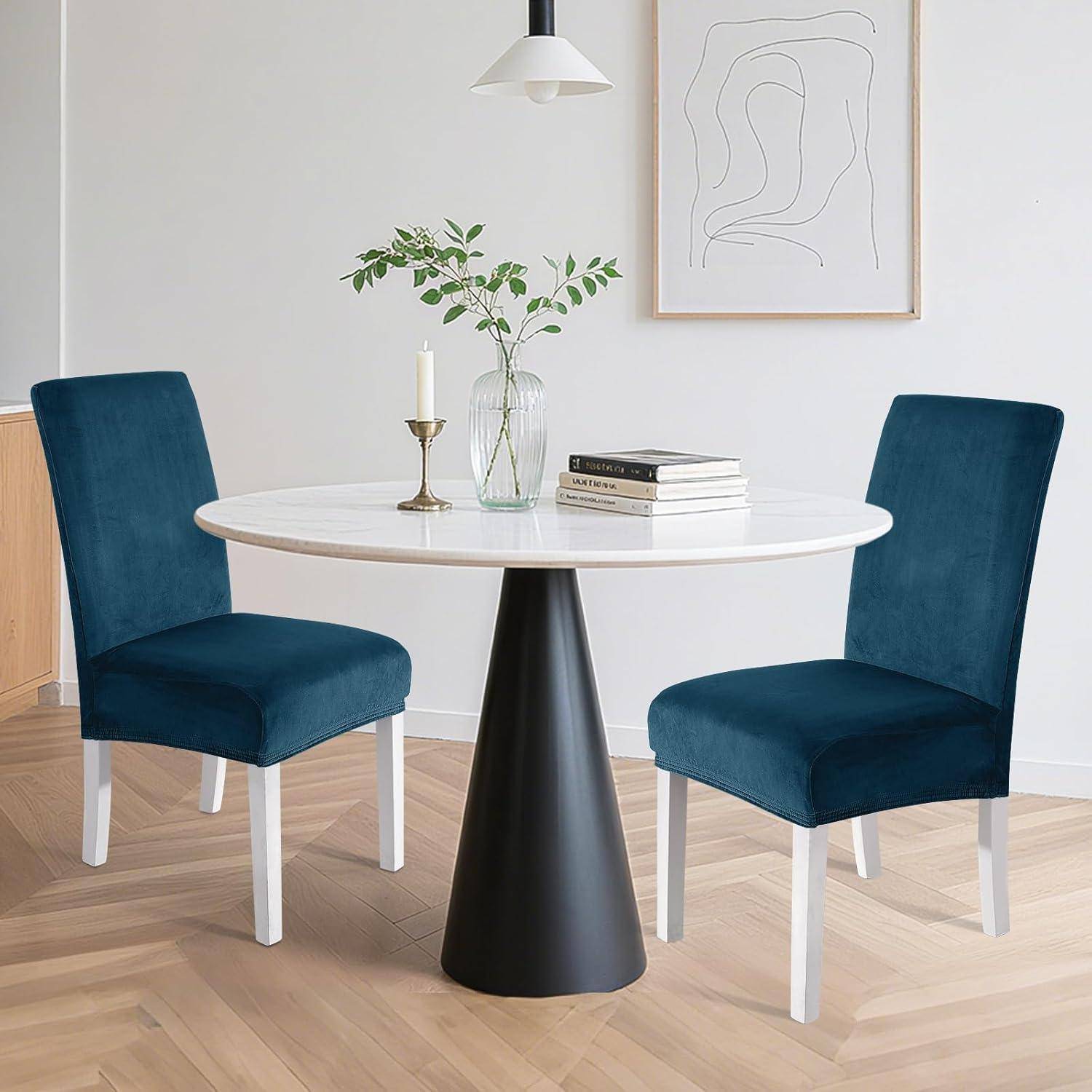 Moderner Essplatz mit rundem weißem Tisch auf schwarzem Sockel, zwei türkisen Stühlen, Vase und Kerze, Bücherstapel und minimalistischer Wandkunst