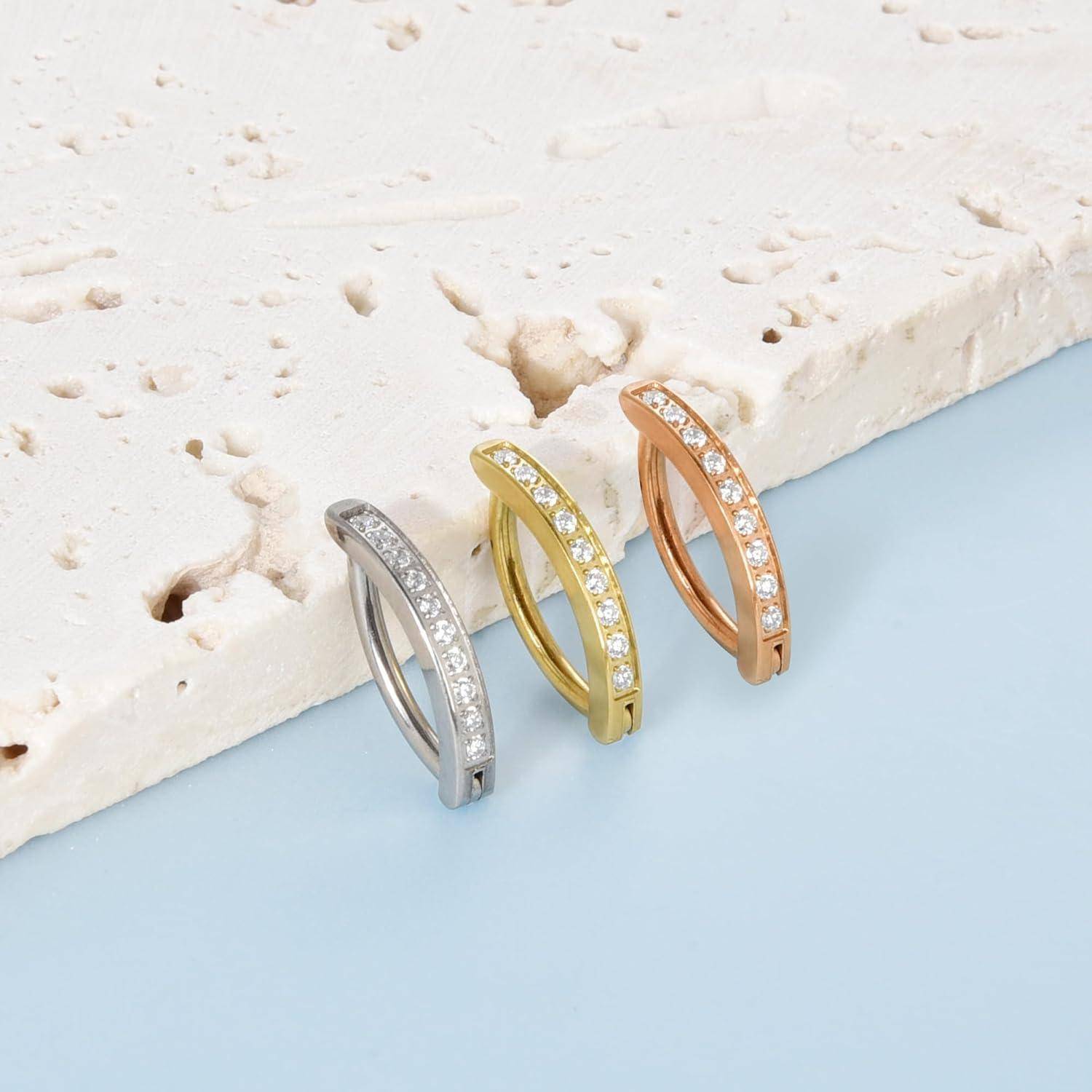 Drei schlanke, mit Edelsteinen besetzte Creolen in Silber, Gold und Roségold auf einer hellblauen Oberfläche neben weißem Stein.