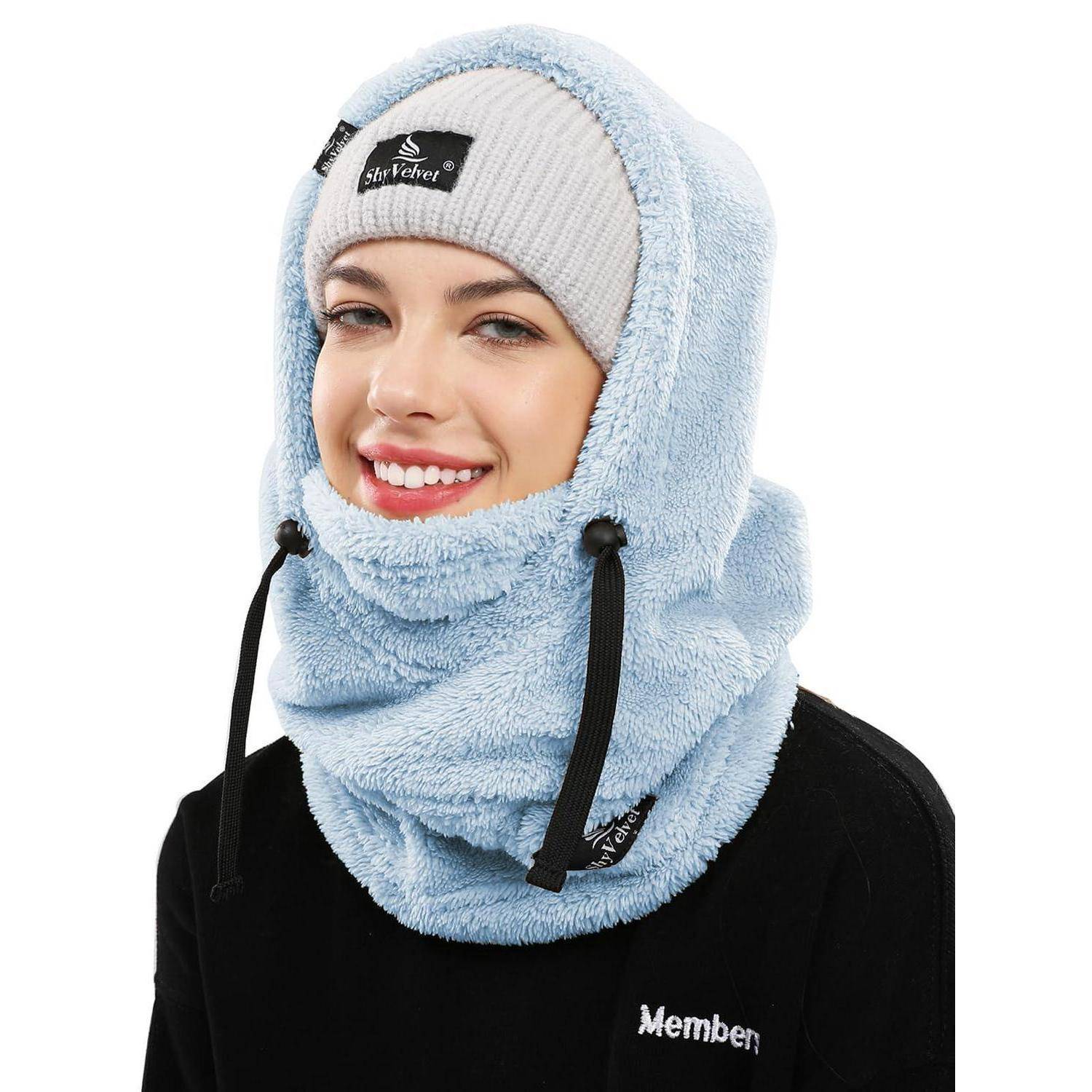 Lächelnde Frau, die eine hellblaue Fleece-Kapuze und eine weiße Beanie trägt, in einem produktähnlichen Porträt vor weißem Hintergrund dargestellt.