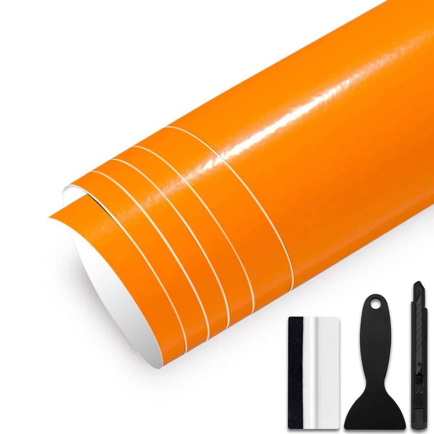 Oranges Vinyl-Wrap-Blatt mit Luftableitungsrillen, plus Schaber, Rakel und Universalmesser auf weißem Untergrund.