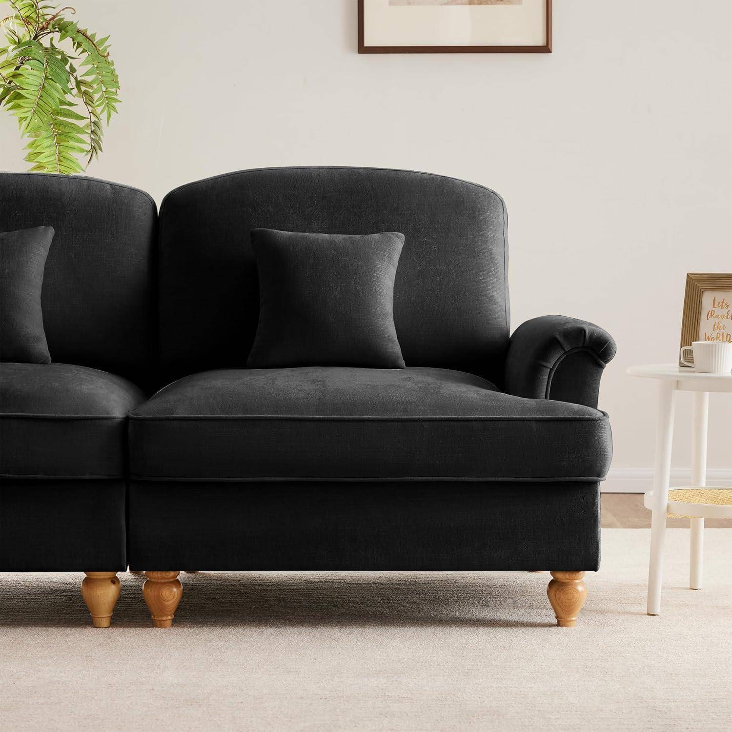 Schwarzes gepolstertes Sofa mit passendem Kissen in einem hellen Wohnzimmer, neben einem kleinen weißen Beistelltisch und einer Pflanze.