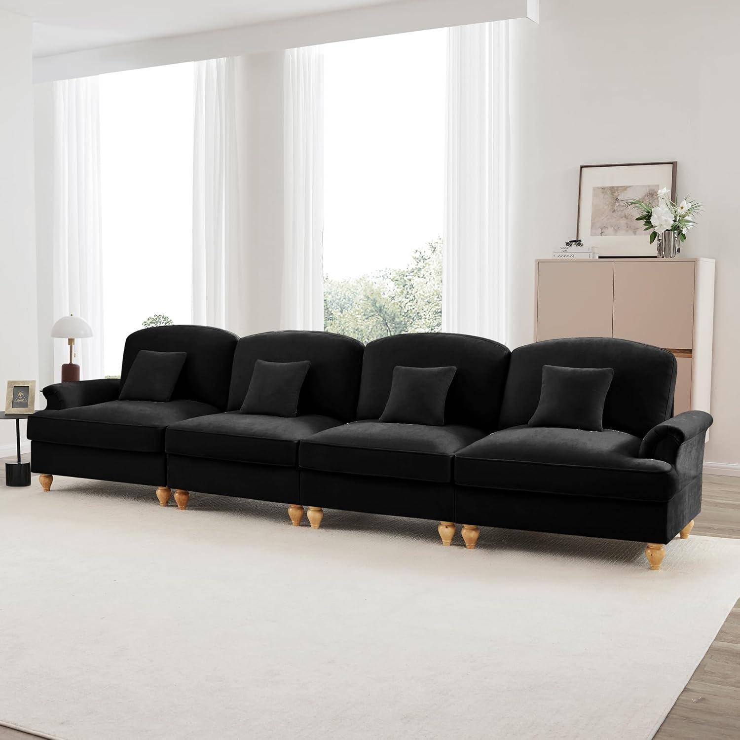 Schwarzes viersitziges Sofa mit passenden Dekokissen in einem hellen, minimalistischen Wohnzimmer mit großen Fenstern und einem hellen Teppich.