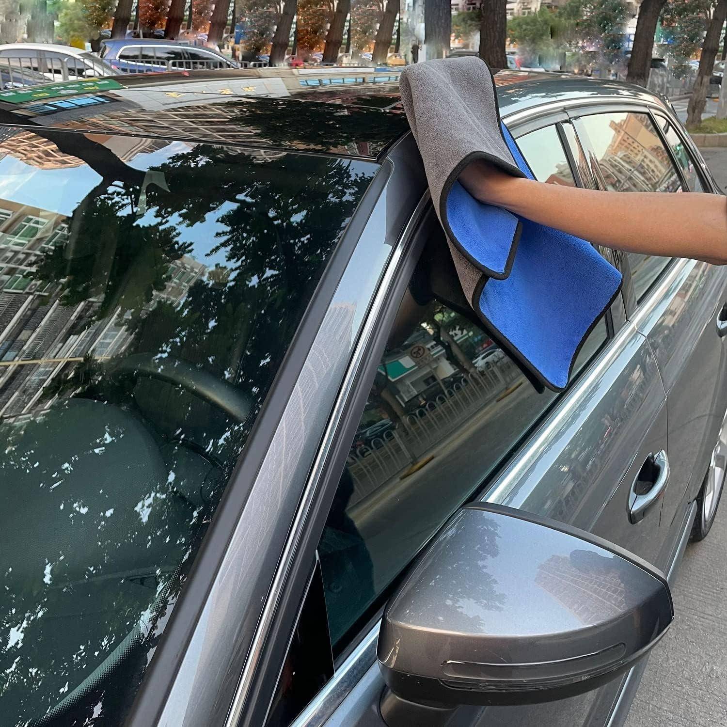 Person, die das Dach und das Seitenfenster eines grauen Autos mit einem Mikrofasertuch auf einer Straße mit geparkten Autos abwischt.