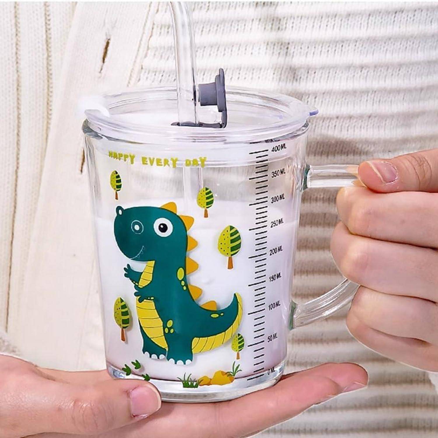 Eine Hand hält einen durchsichtigen 400-ml-Messbeucher mit einem Dinosaurier-Muster, während Wasser hineingewissert wird.