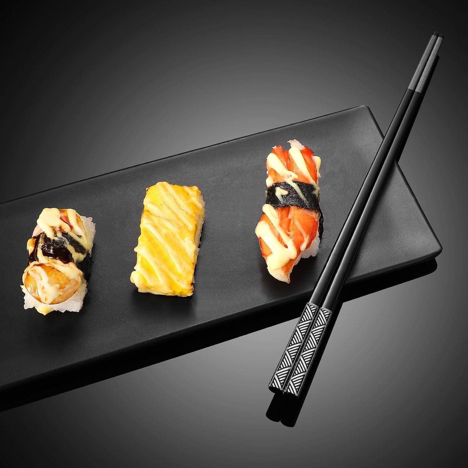 Drei Sushi-Stücke auf einem schwarzen rechteckigen Teller mit schwarzen Essstäbchen, arrangiert auf einem dunklen Hintergrund.