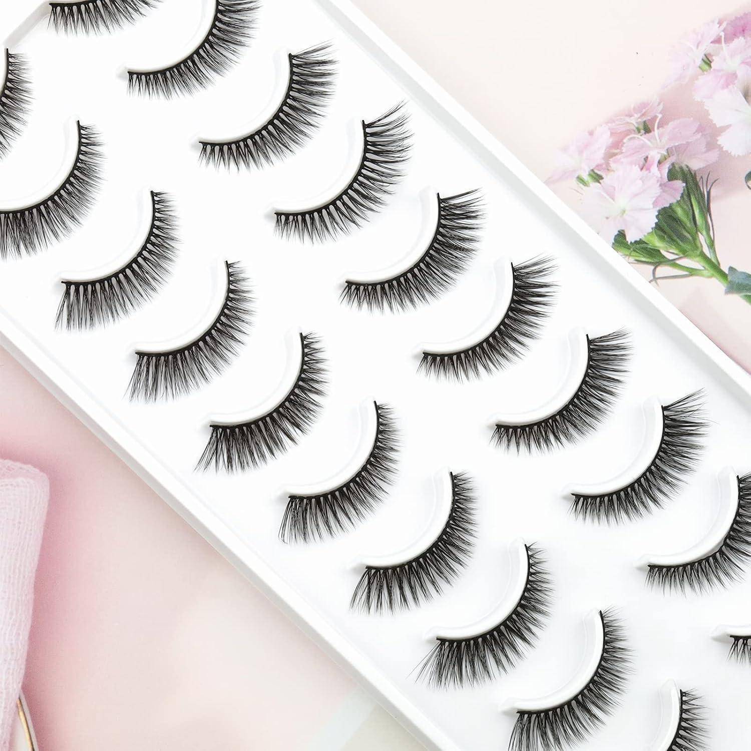 Verschiedene künstliche Wimpern, angeordnet in einem weißen Präsentationstablett auf einem sanften rosa Hintergrund.