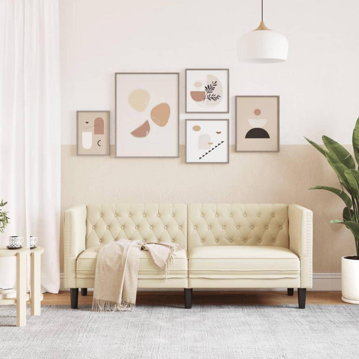 Stilvolles Wohnzimmer mit cremefarbigem Polstersofa mit Steppung, abstraktem Bilderrahmen, Pendelleuchte, Teppich und Topfpflanze in einem hellen, neutralen Raum.