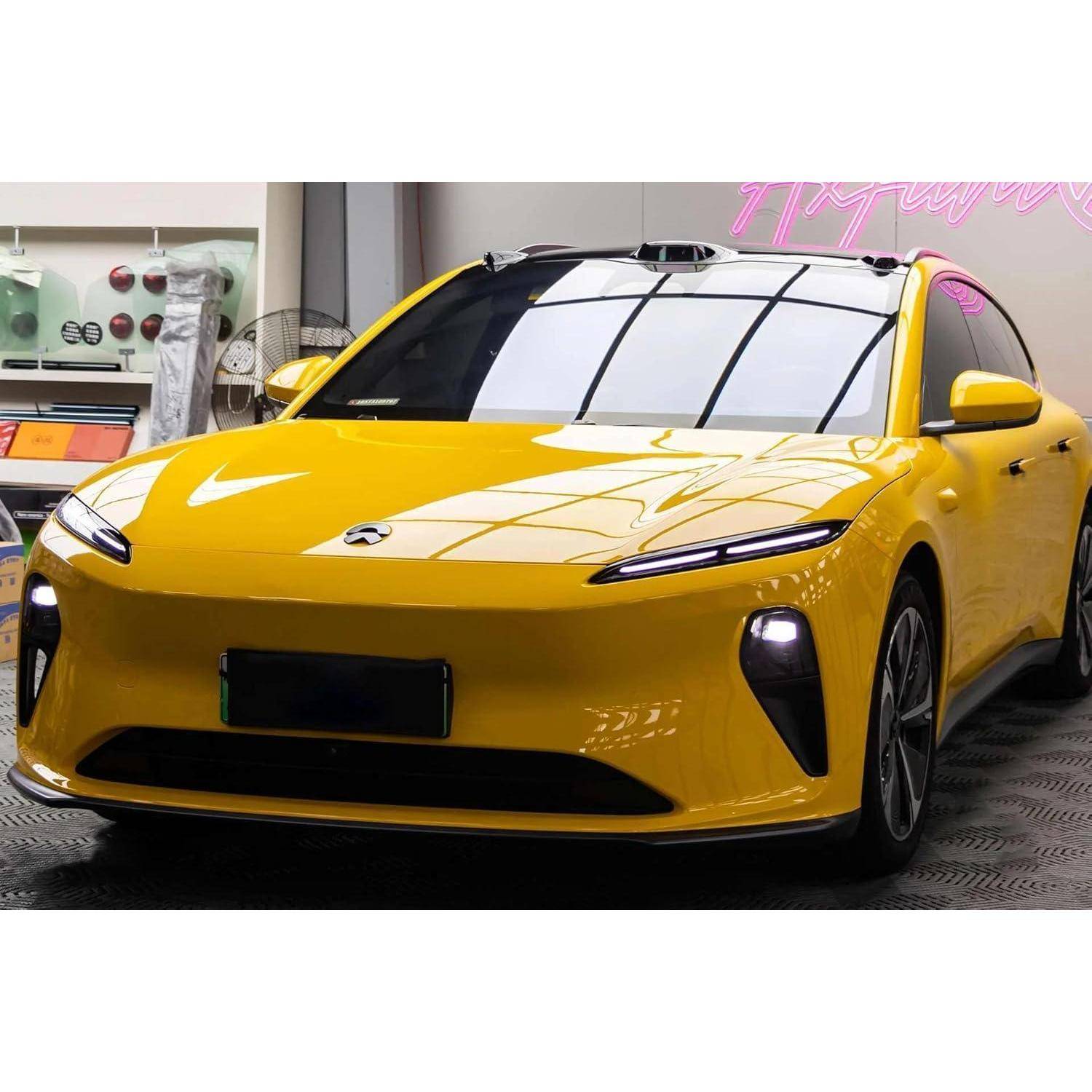 Helles gelbes Elektroauto in einer Ausstellungshalle, Frontansicht mit eleganten Scheinwerfern und schwarzen Verzierungen.
