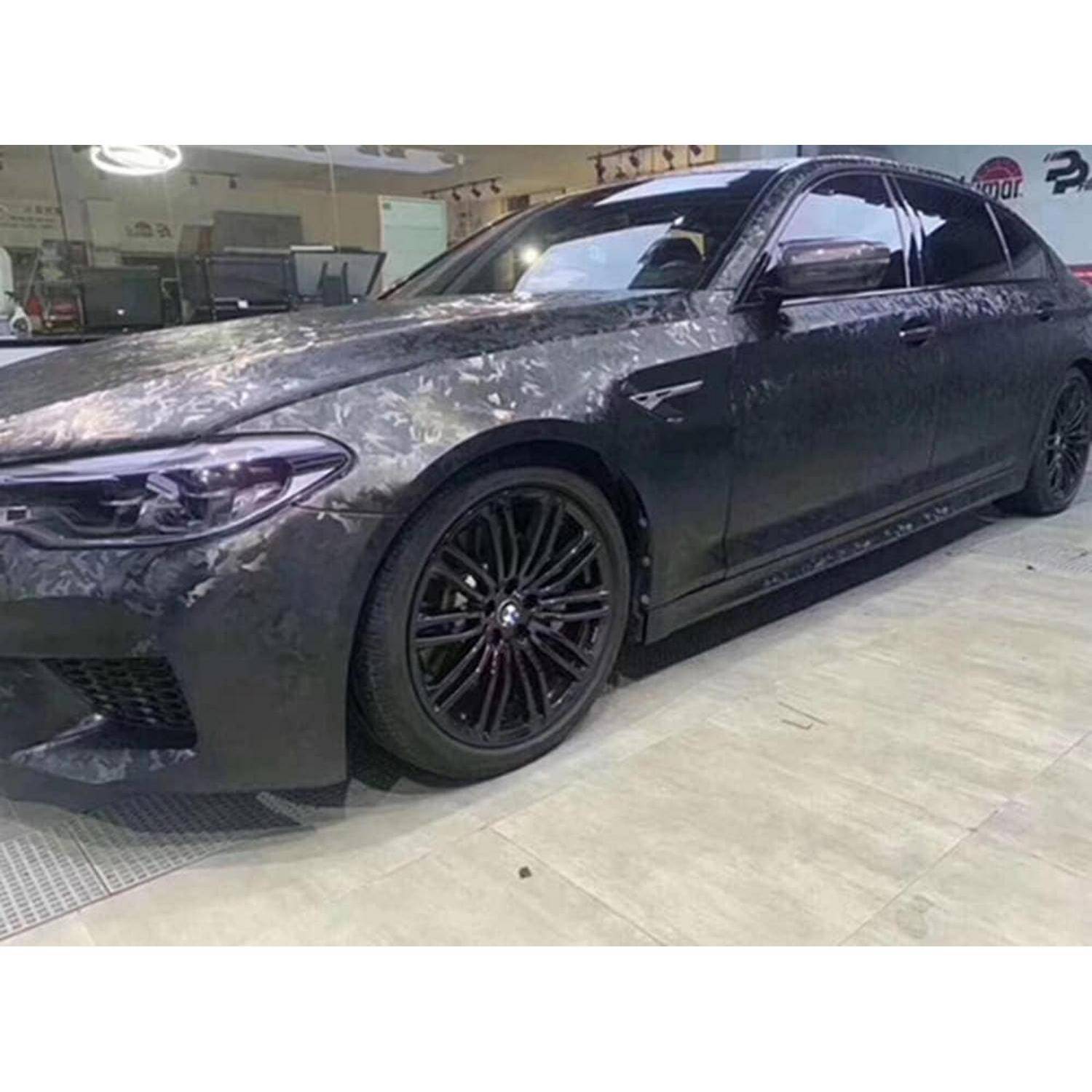 Dunkelgrauer BMW-Limousine mit Tarnanstrich-Folie und schwarzen Felgen in einer Garage oder Werkstatt drinnen geparkt.