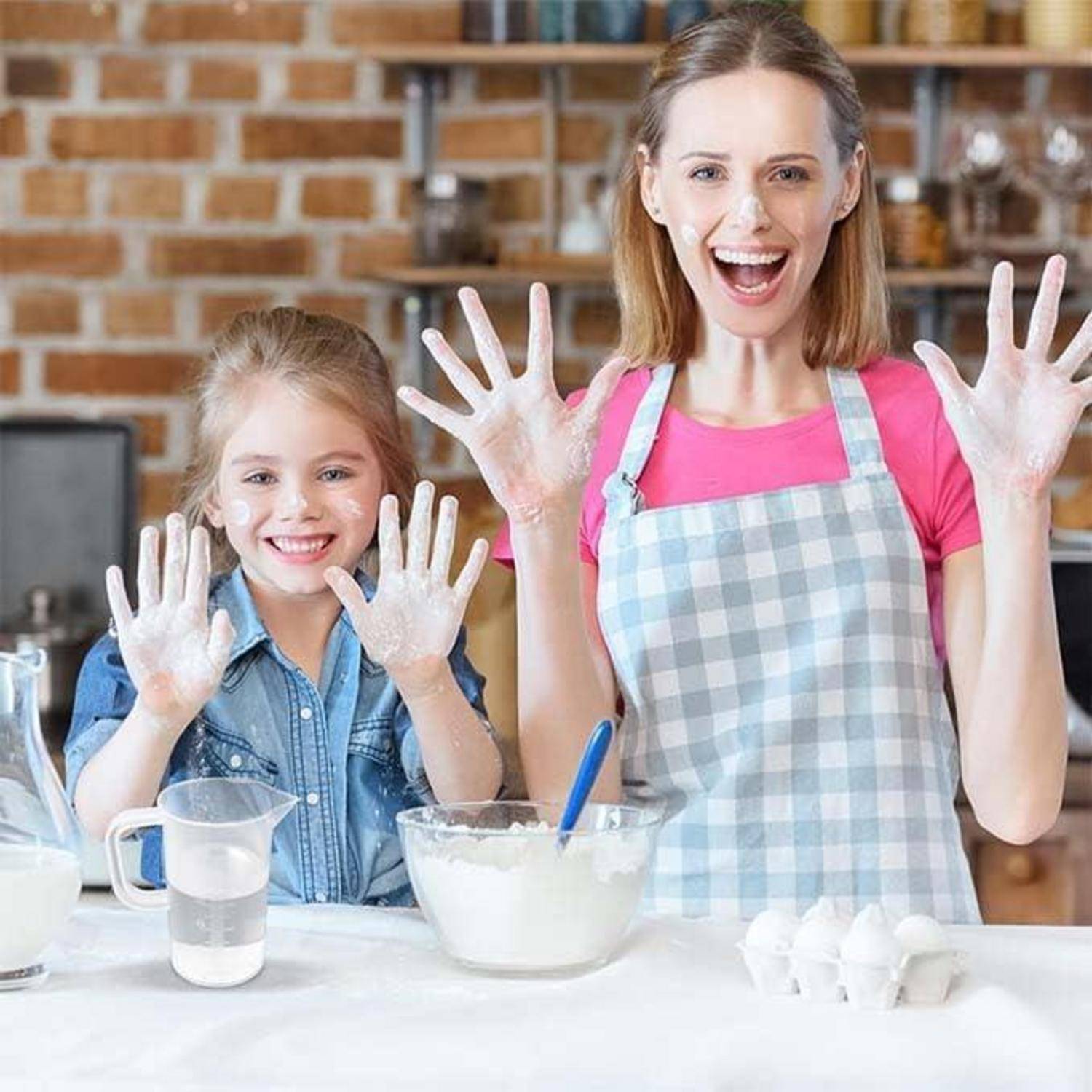Mutter und Tochter in einer Küche, lächelnd mit mehlbedeckten Händen beim Backen; Schüssel, Messbecher und Eier auf der Arbeitsplatte.