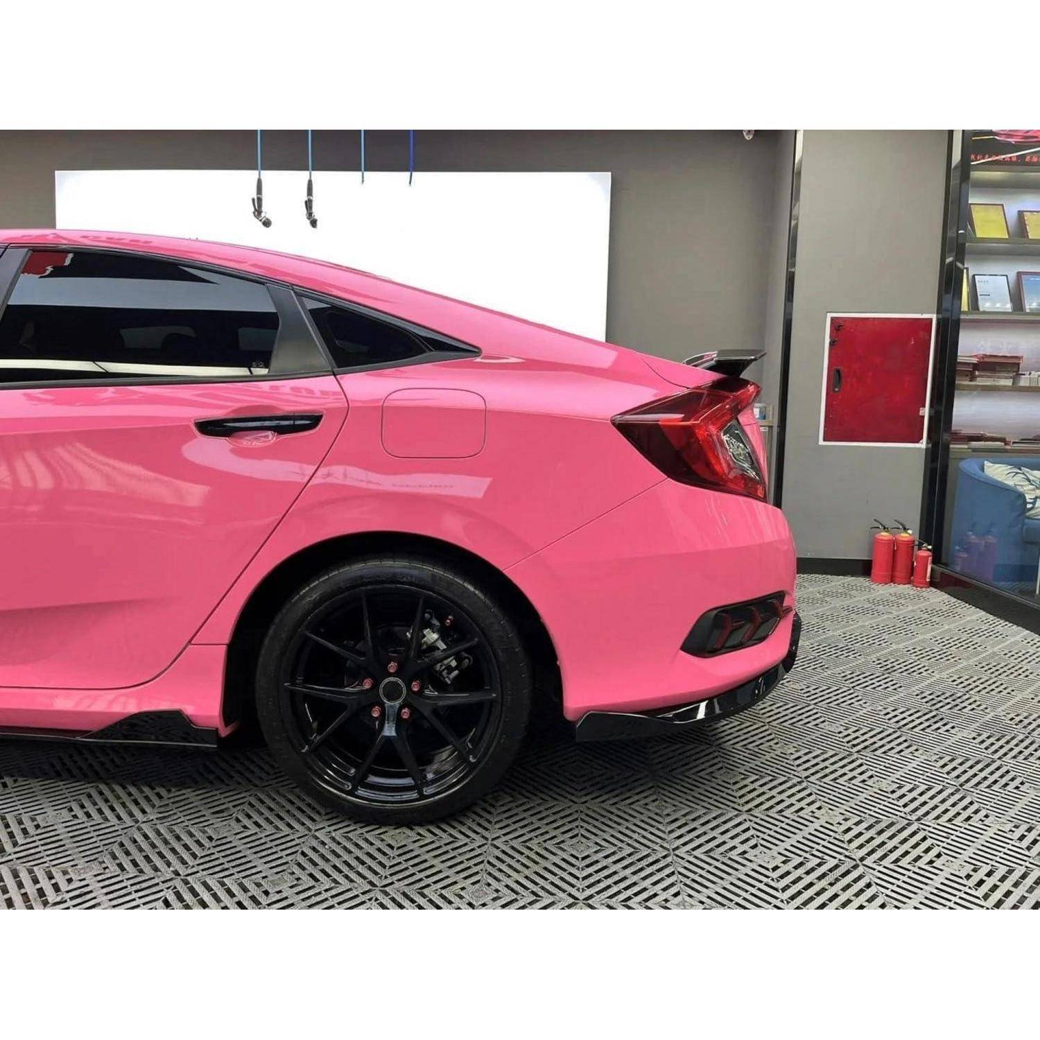 Rosa Coupéauto in einer Garage oder in einem Ausstellungsraum geparkt, von der Seite und von hinten dargestellt, mit schwarzen Rädern.