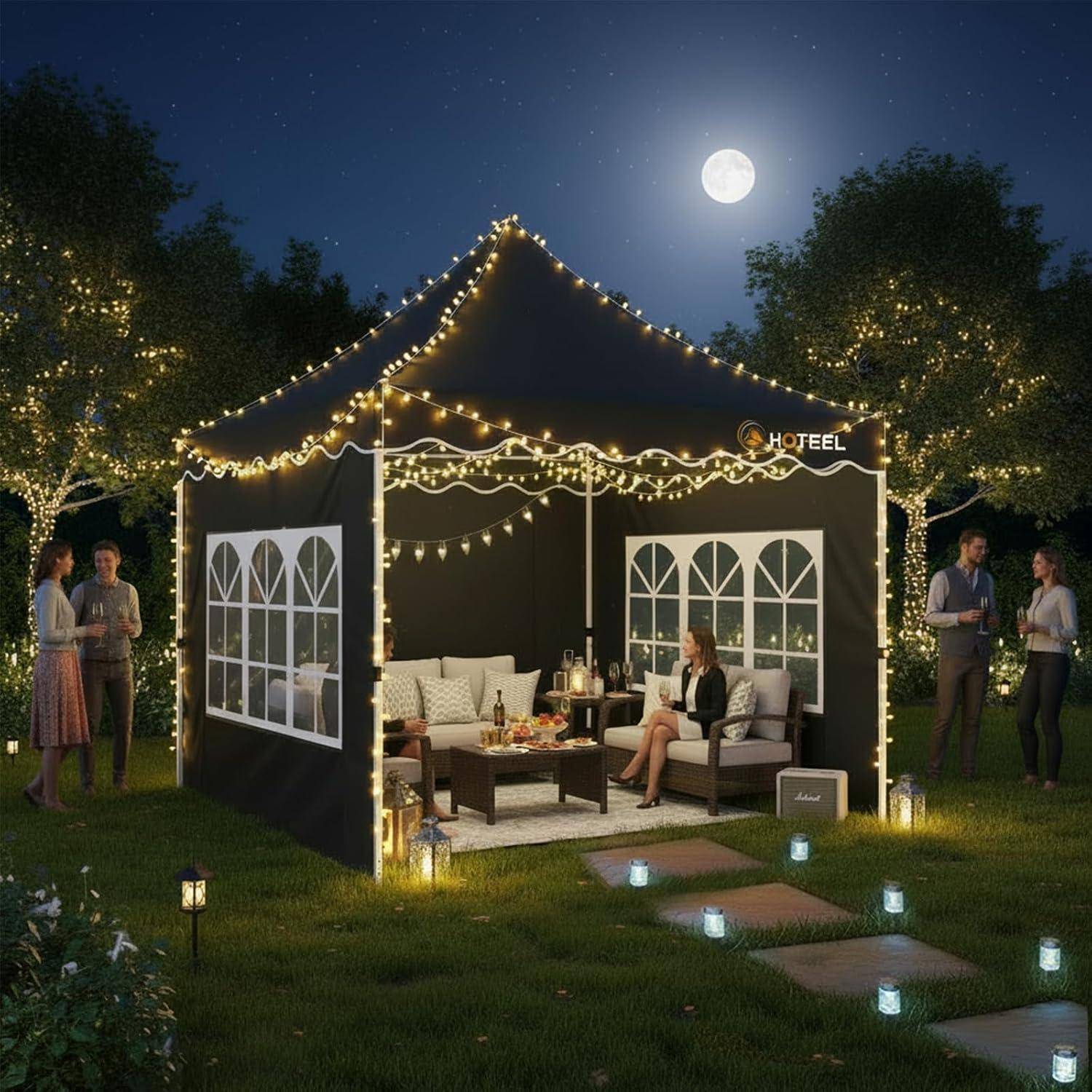 Mondbeleuchtete Hotelterrasse im Freien mit Festzelten, Lichterketten, Sitzgelegenheiten und Gästen, die auf einem Rasen plaudern, mit beleuchteten Trittsteinen.