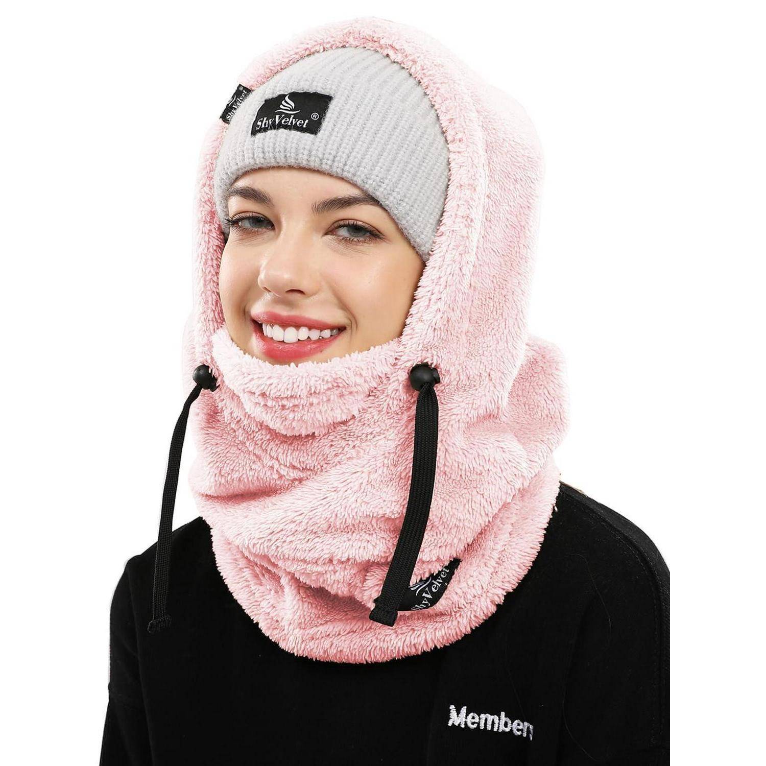 Lachende Frau, die eine rosa Fleece-Kapuze und eine graue Mütze mit einem schwarzen Sweatshirt vor weißem Hintergrund trägt.