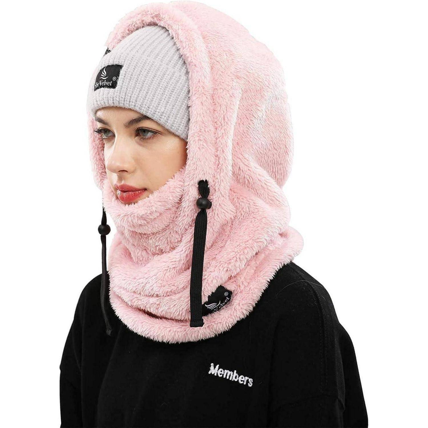 Frau, die eine rosa Fleece-Kapuze und einen Nackenwärmer über einer grauen Beanie und einem schwarzen Sweatshirt trägt, gezeigt im Profil vor weißem Hintergrund.