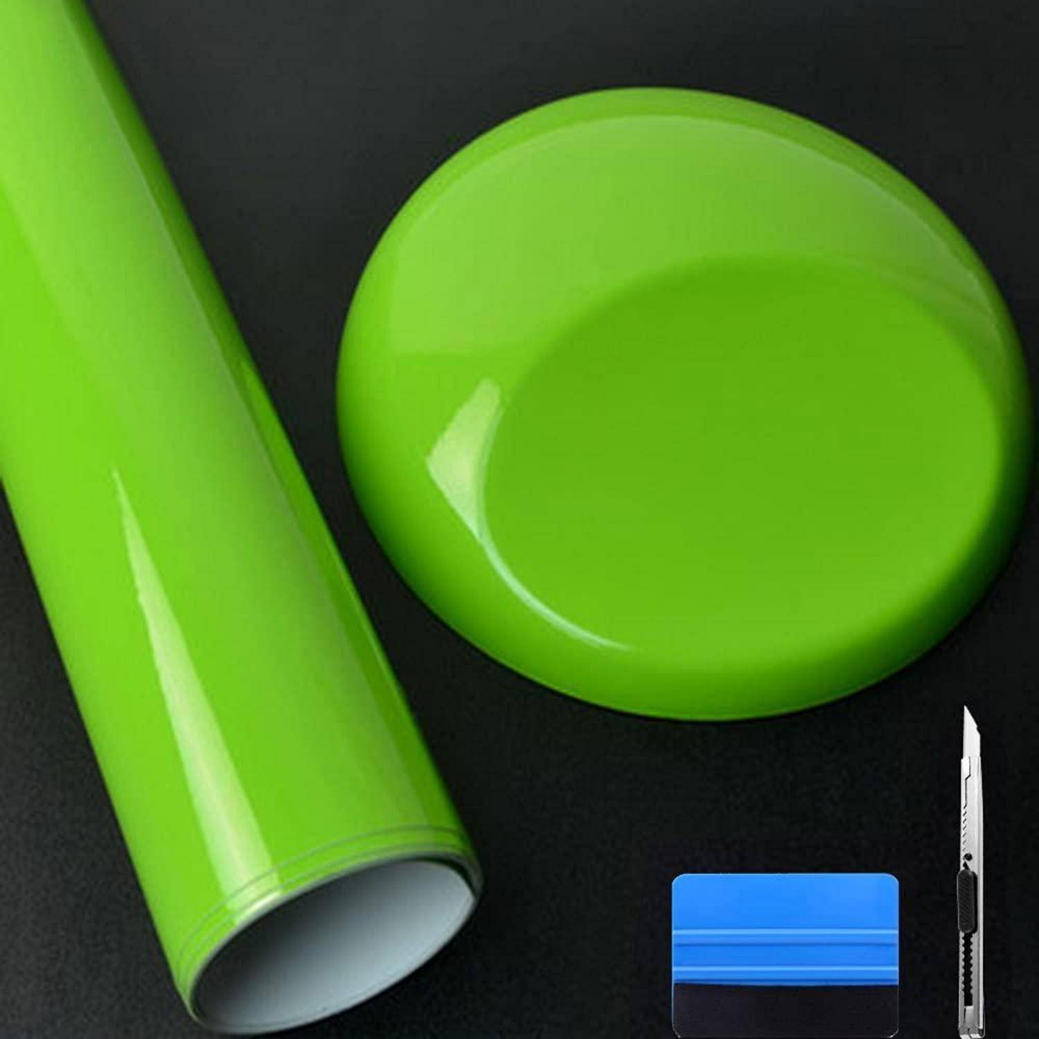 Grüne Klebstoffvinylrolle, passender runder Aufkleber und Universalmesser auf schwarzem Hintergrund, was auf Schild- oder Bastelmaterialien hindeutet.