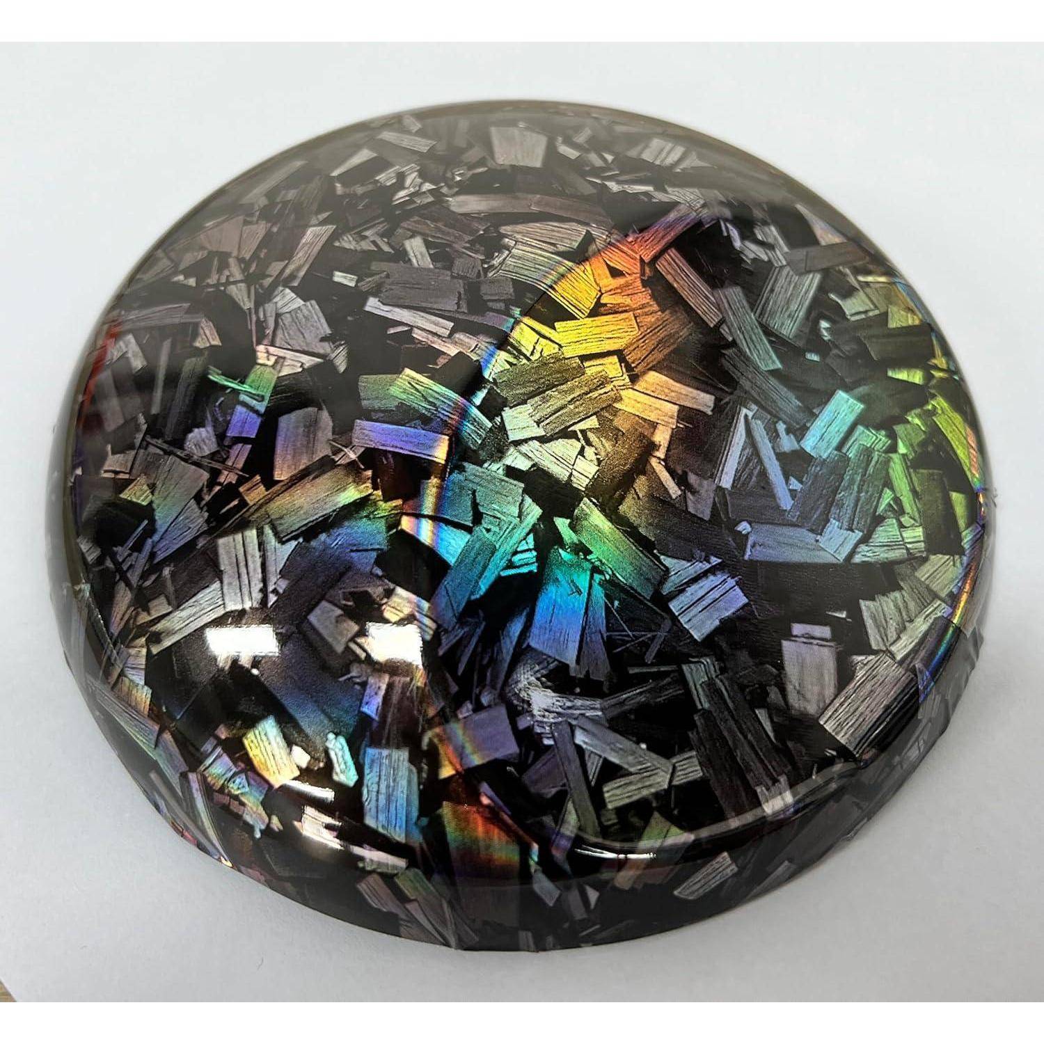 Nahaufnahme eines glänzend schwarzen irisierenden runden Edelsteins oder Cabochons mit mehrfarbigen reflektierenden Flöckchen auf weißem Hintergrund.