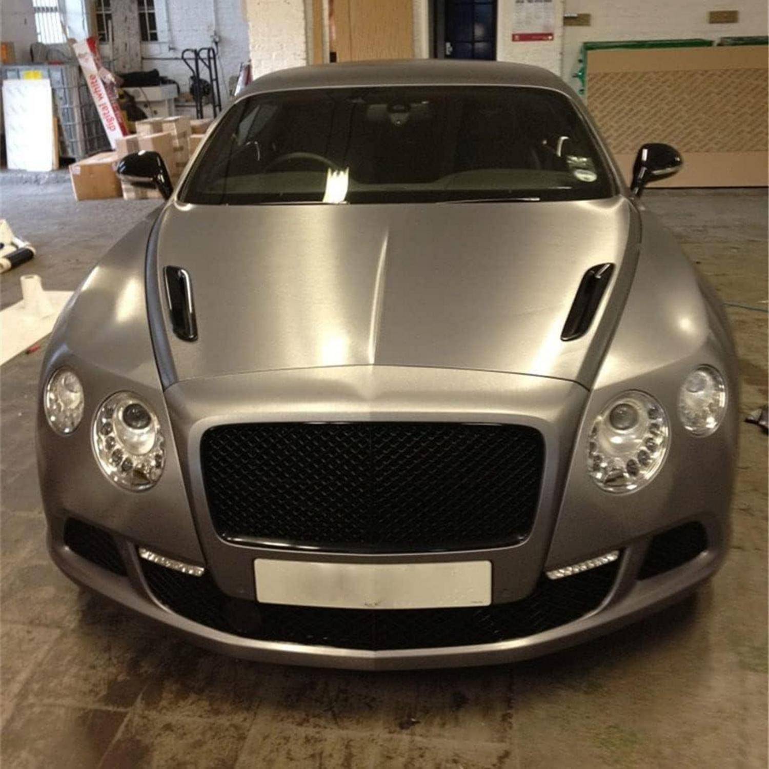Vorderansicht eines silbernen Bentley-Coupés, das drinnen geparkt ist und einen großen schwarzen Kühlergrill und runde Scheinwerfer zeigt.