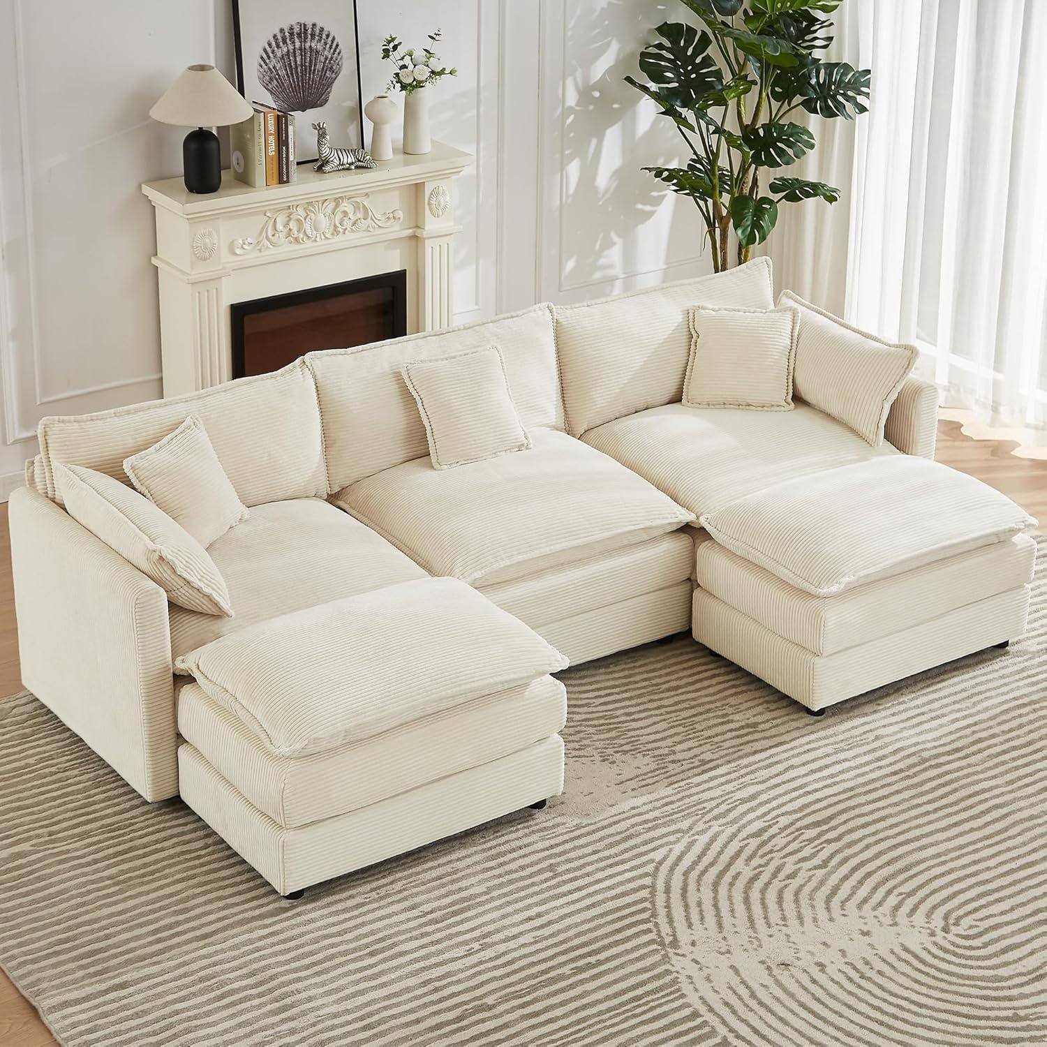 Cremefarbiges Ecksofa mit ottomanischen Sitzen und Kissen in einem hellen Wohnzimmer neben einem Kamin und einem großen Fenster.