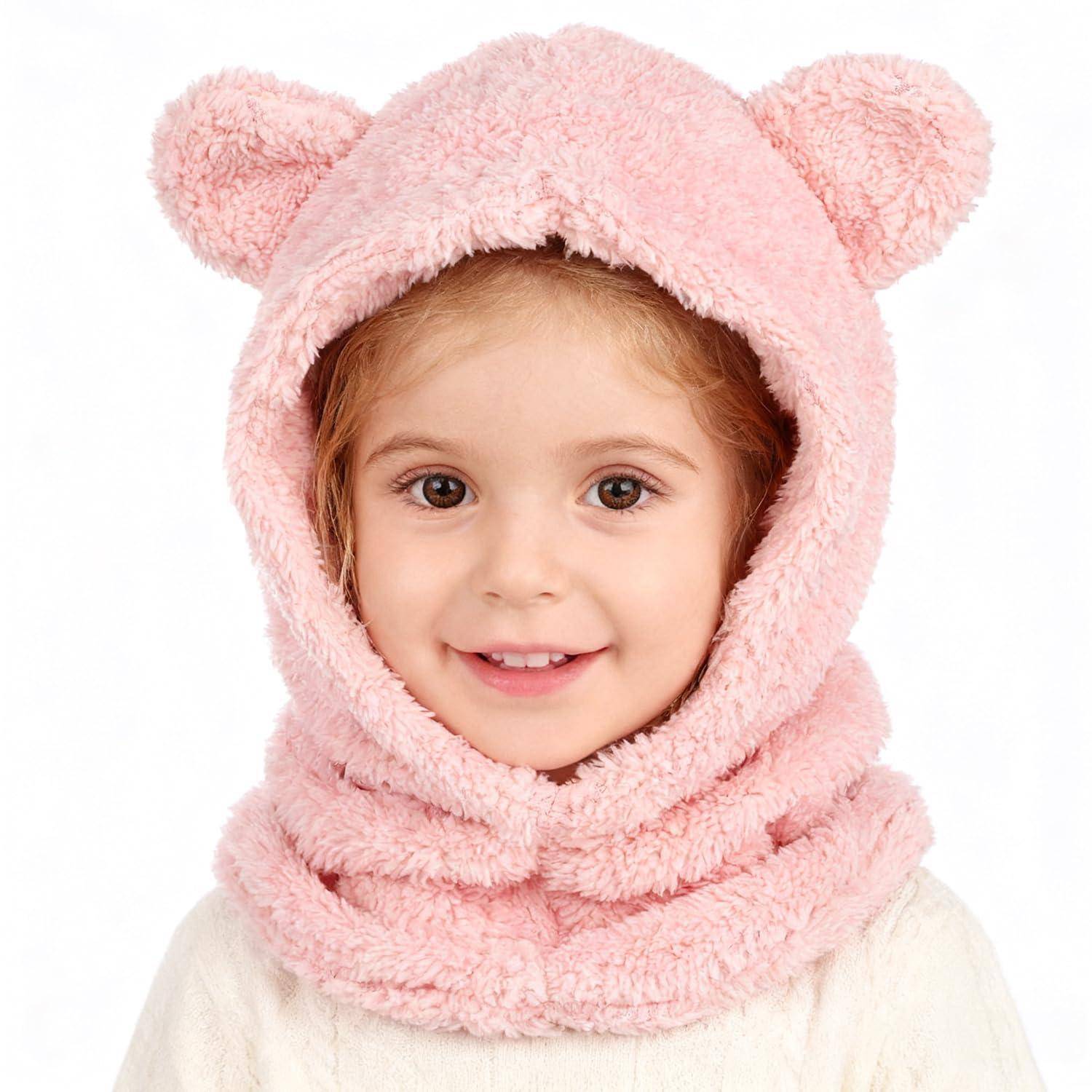 Lachendes kleines Kind in einer rosa flauschigen Kapuze mit Bärenohren, frontal vor weißem Hintergrund.
