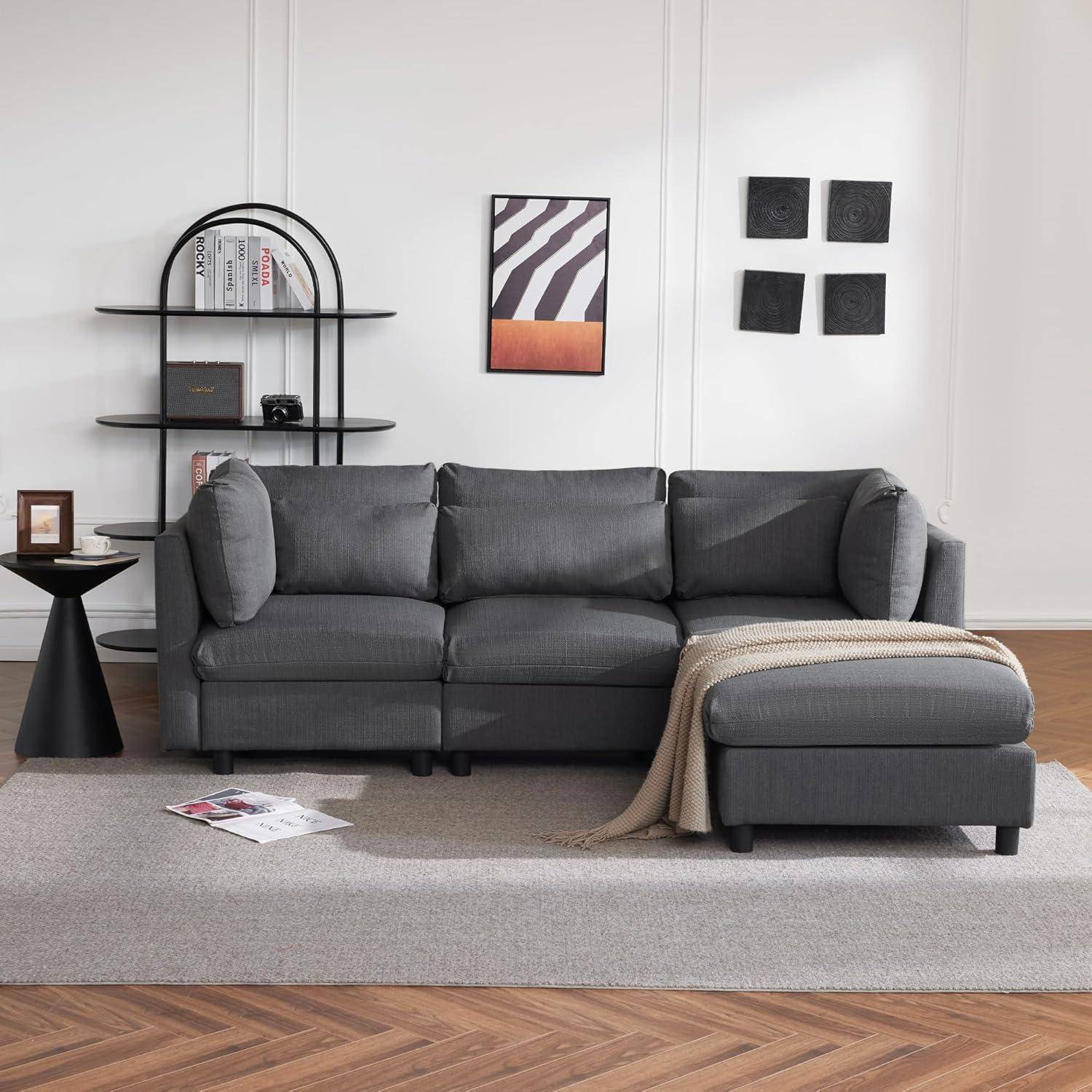 Modernes Wohnzimmer mit dunkelgrauem Ecksofa, schwarzen Wandregalen und rahmengeometrischer Kunst auf einem hellen Teppich über einem Fischgrätenmuster-Holzboden.